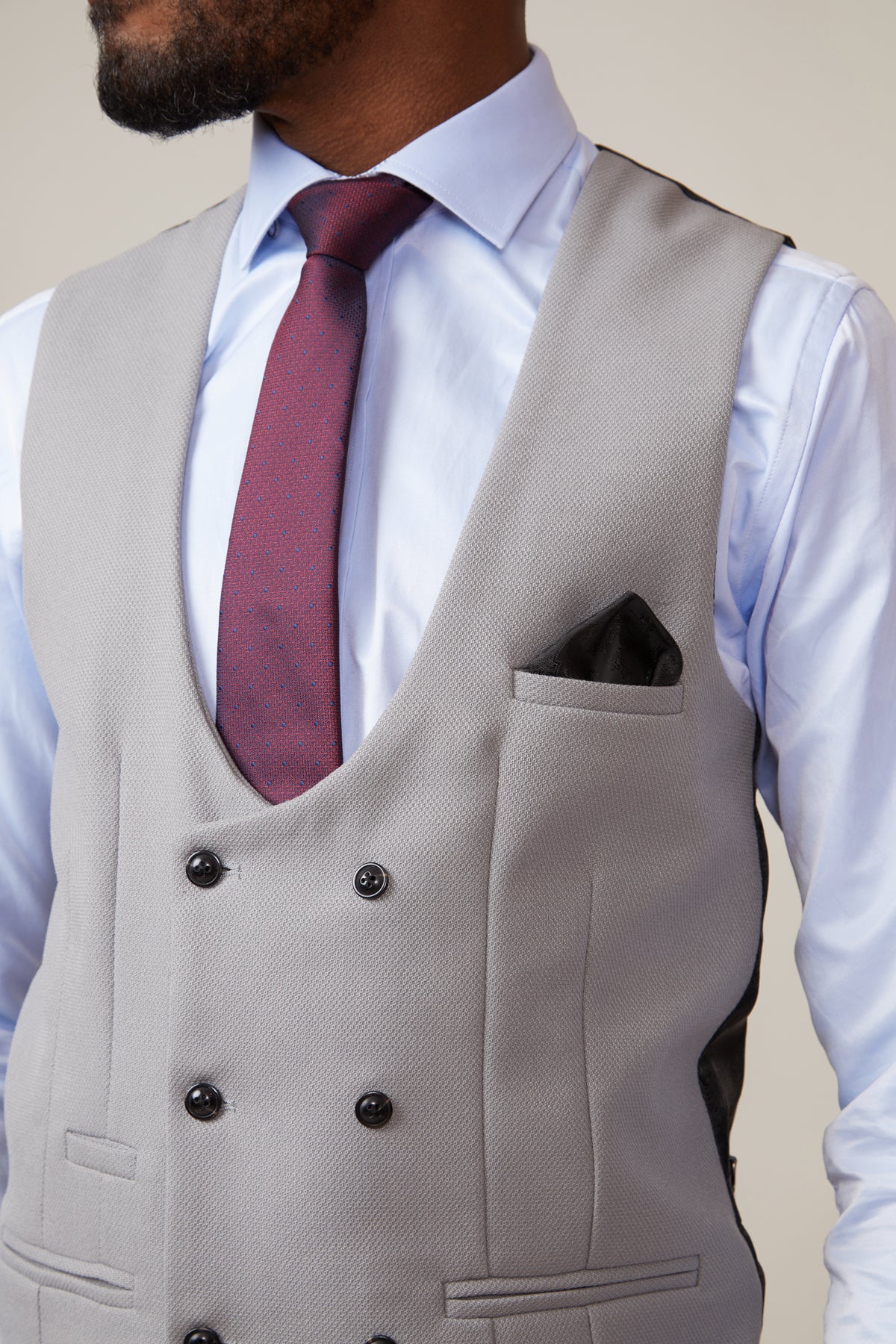 A man wears the marcdarcy KELVIN Silver Double Breasted Waistcoat, paired with a pale blue shirt, burgundy tie, and black pocket square. His face is partially visible and he has a beard.