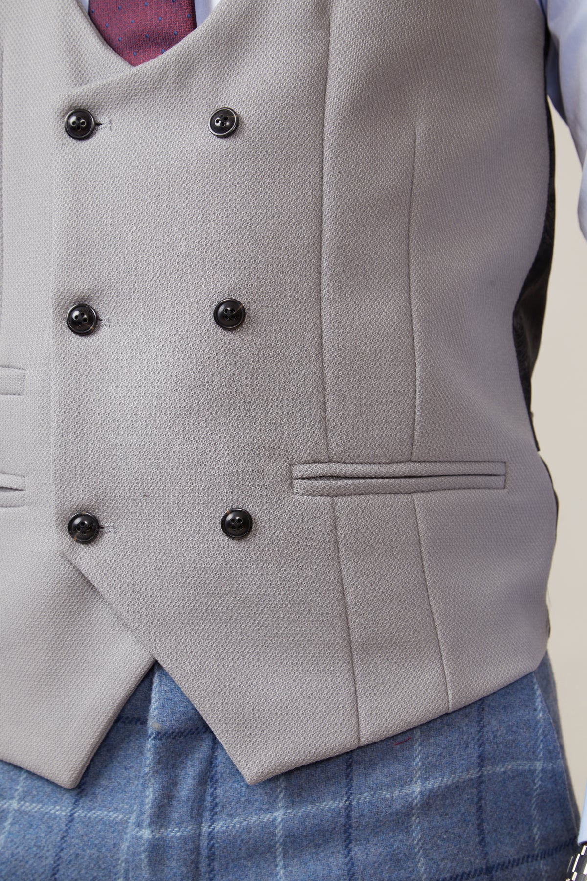 Close-up of a person wearing the marcdarcy KELVIN Silver Double Breasted Waistcoat with black buttons, styled with a maroon tie, white shirt, and blue plaid trousers. The focus is on the waistcoat and lower torso.