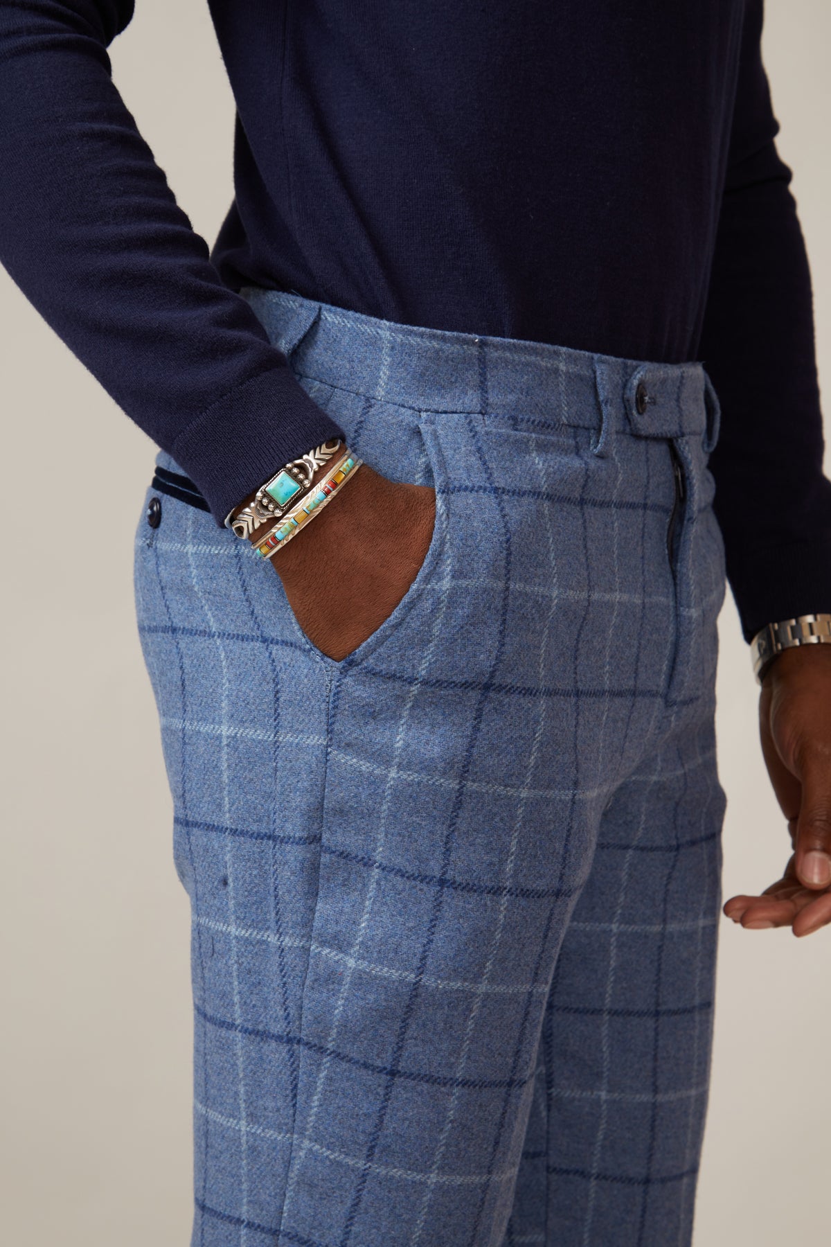 A person stands with one hand in their pocket, showcasing bracelets and a wristwatch while wearing marcdarcy’s CLINTON - Blue Tweed Check Trousers.