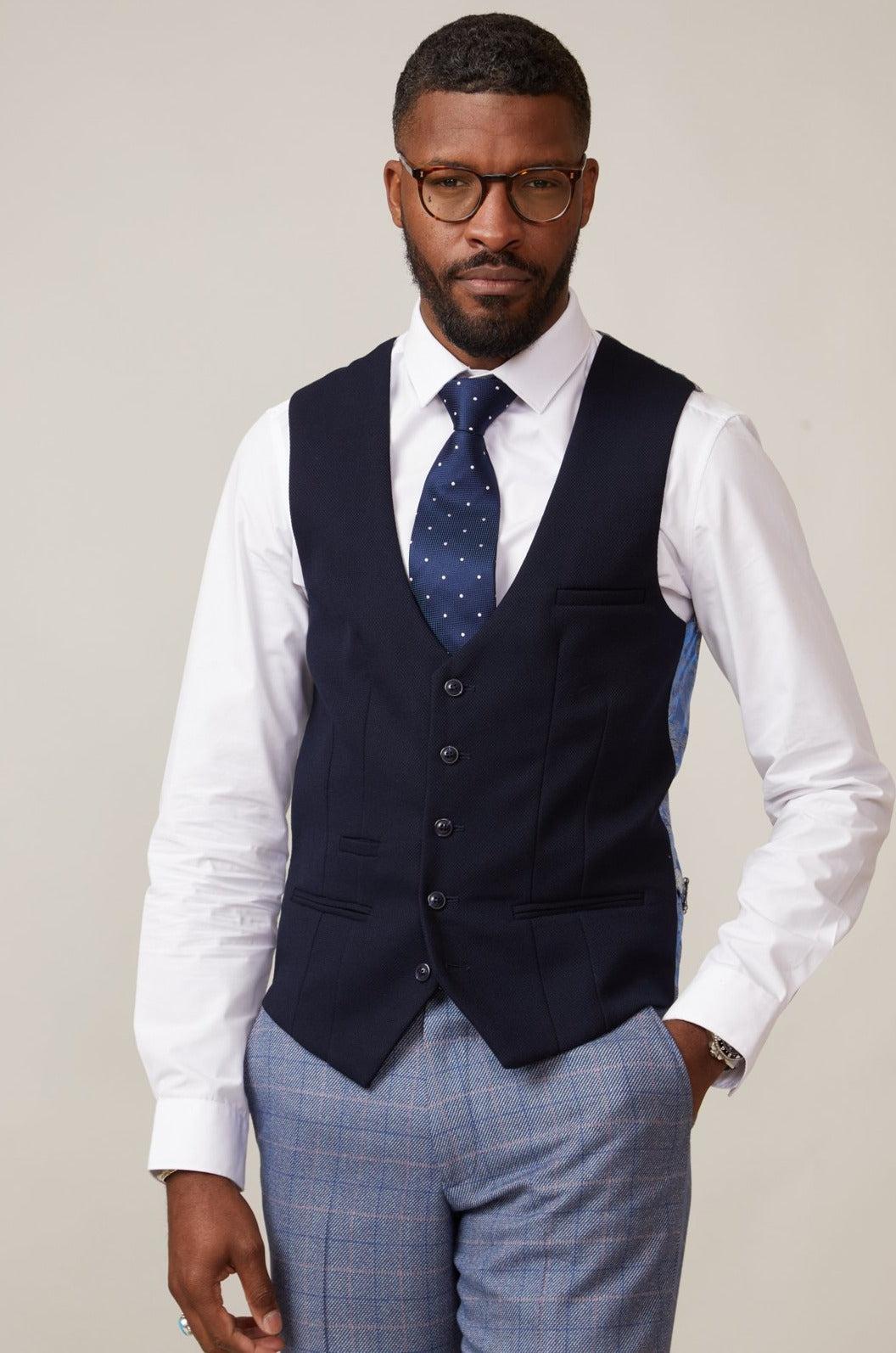 A Black man wearing glasses, a white shirt, navy polka dot tie, the marcdarcy KELVIN - Navy Single Breasted Waistcoat, and blue checkered pants—a sharp formal look for any occasion.