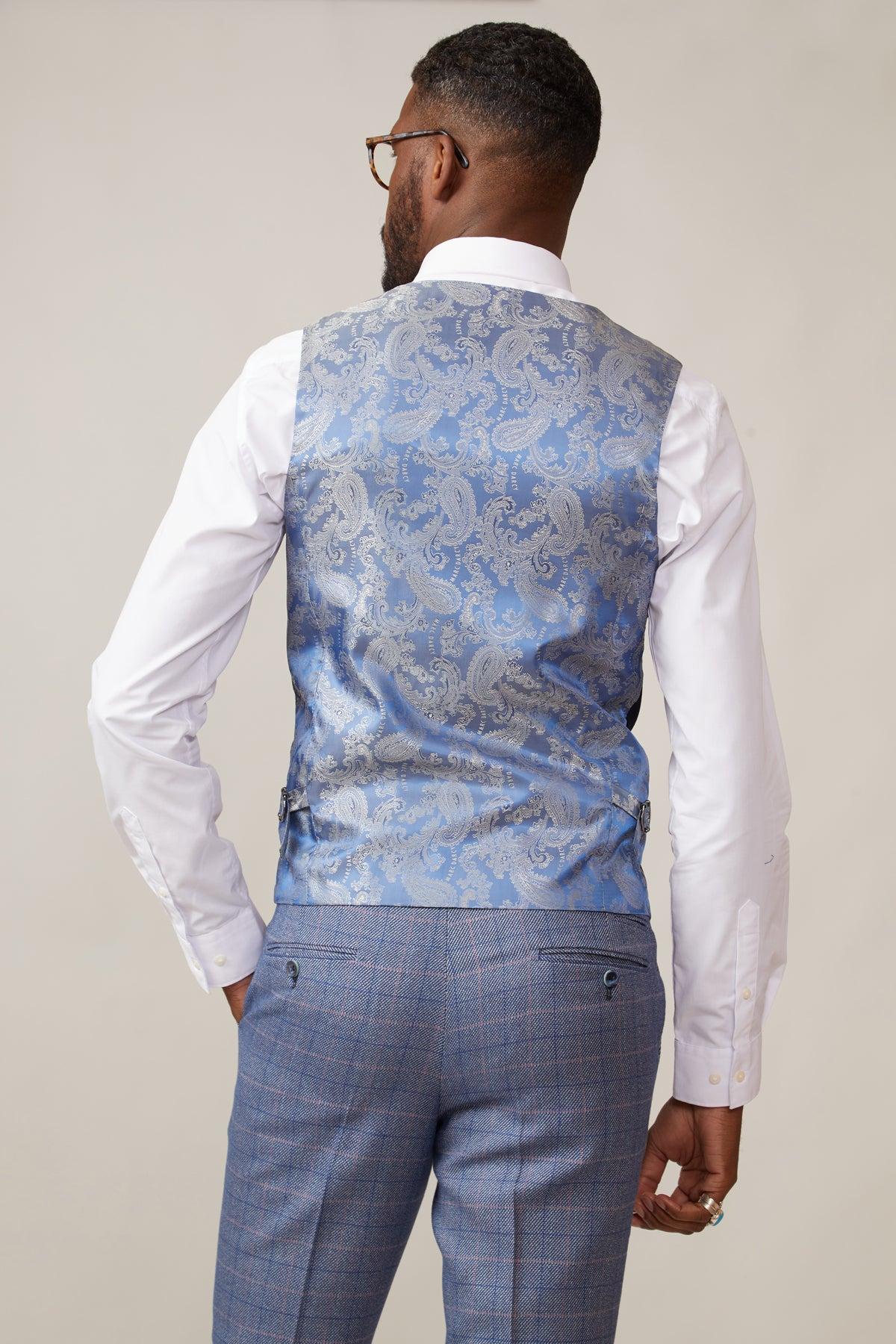 A man with short hair, a trimmed beard, and glasses models the marcdarcy KELVIN navy single-breasted waistcoat over a white shirt and blue plaid slim fit trousers. He faces away against a plain light background.
