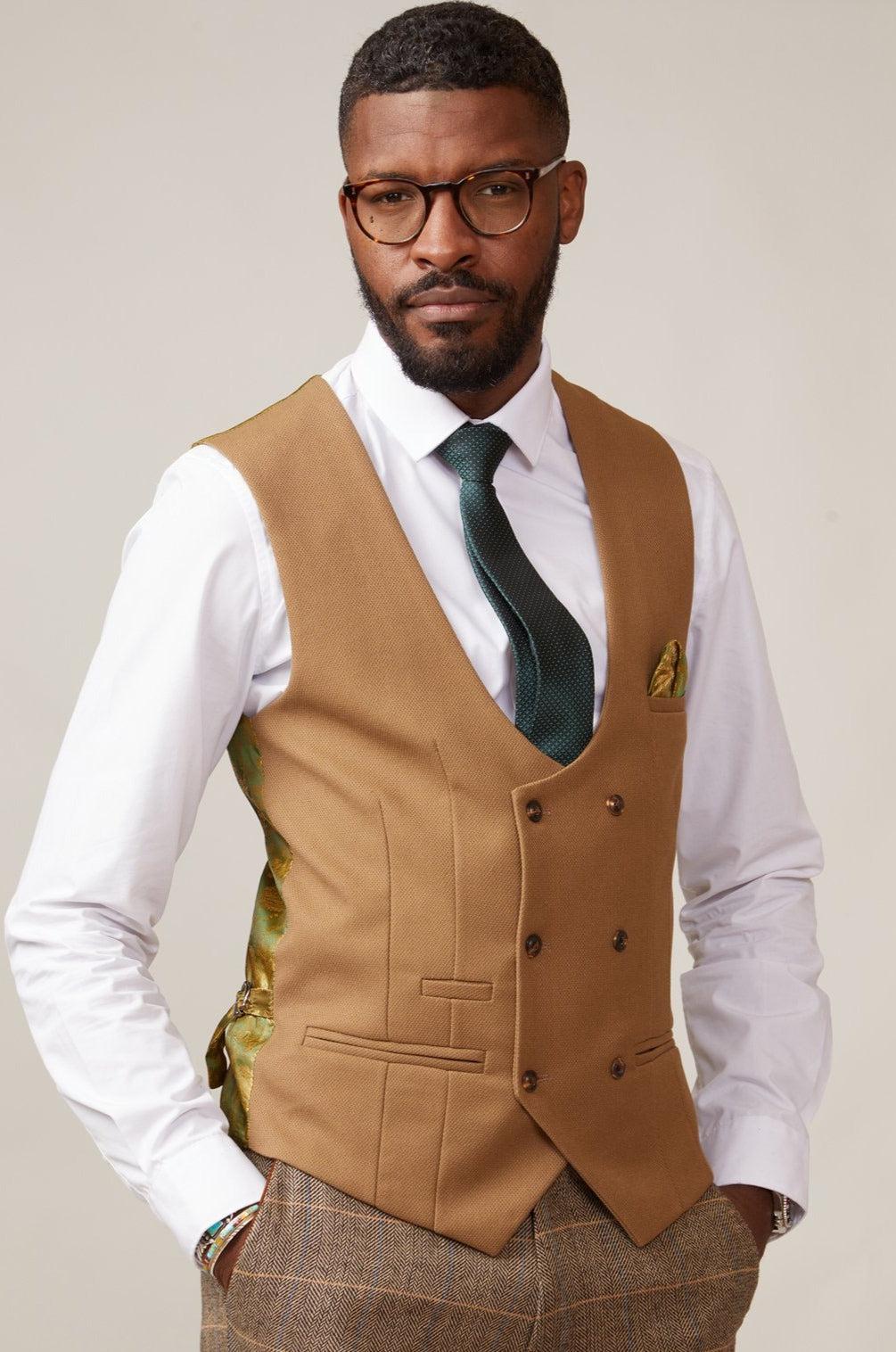 A man with short hair and a beard wears glasses, a white shirt, green tie, and the marcdarcy KELVIN - Oak Double Breasted Waistcoat featuring paisley print lining and a pocket square. Hands in pockets, he looks confidently at the camera.