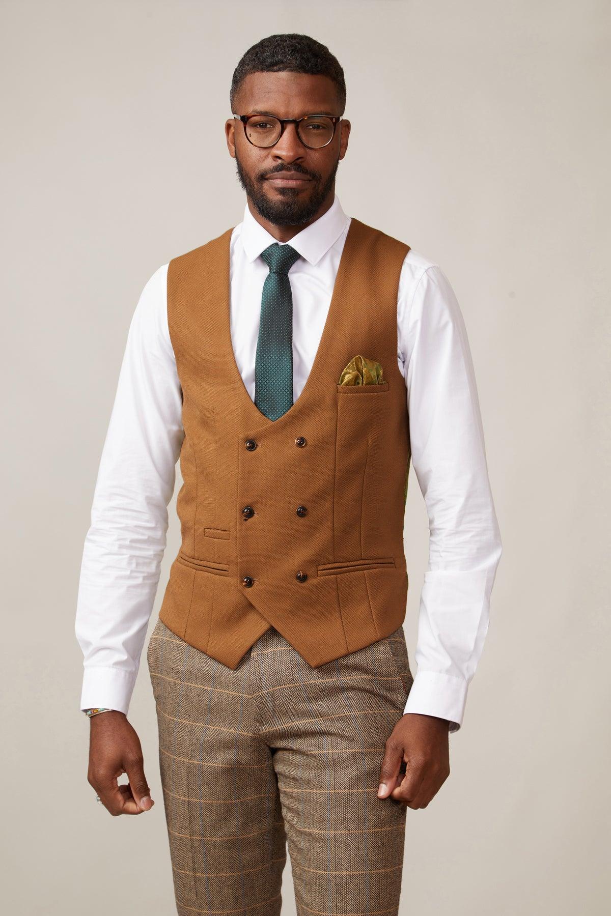 A Black man with glasses and a beard wears a white dress shirt, teal tie, gold pocket square, plaid pants, and the marcdarcy KELVIN Tan Double Breasted Waistcoat.