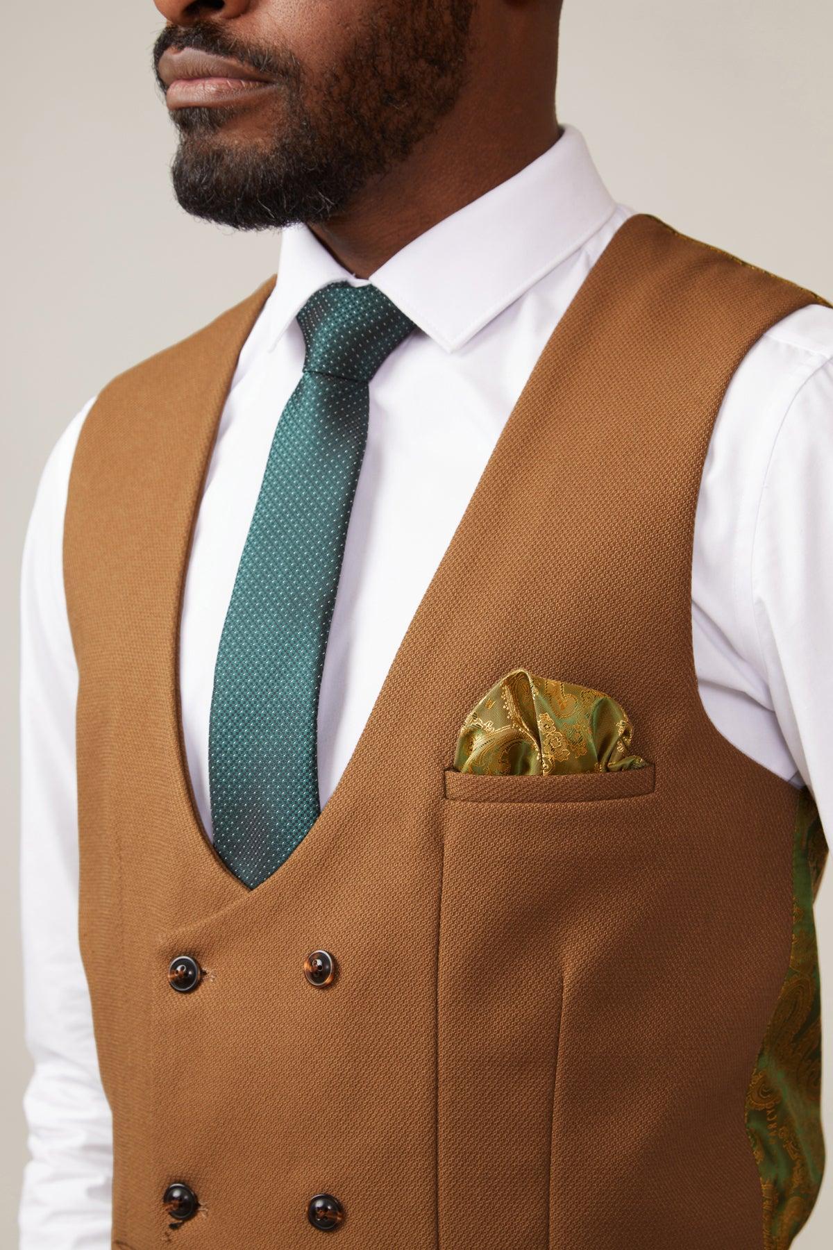 A man wears the marcdarcy KELVIN Tan Double Breasted Waistcoat over a white dress shirt, styled with a green tie and patterned pocket square. The image is cropped to his torso and lower face.