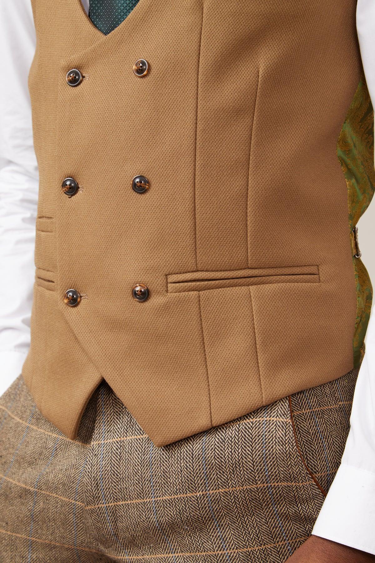 A close-up of a person in the marcdarcy KELVIN - Oak Double Breasted Waistcoat over a white shirt, paired with brown herringbone trousers and a green tie. The elegant paisley print lining is also visible.
