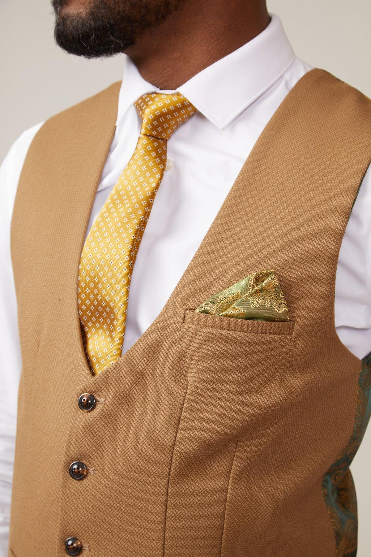 A man wears the marcdarcy KELVIN - Oak Single Breasted Waistcoat over a white dress shirt, paired with a yellow patterned tie and gold pocket square. Only the lower half of his face and trimmed beard are visible, highlighting his tailored style.