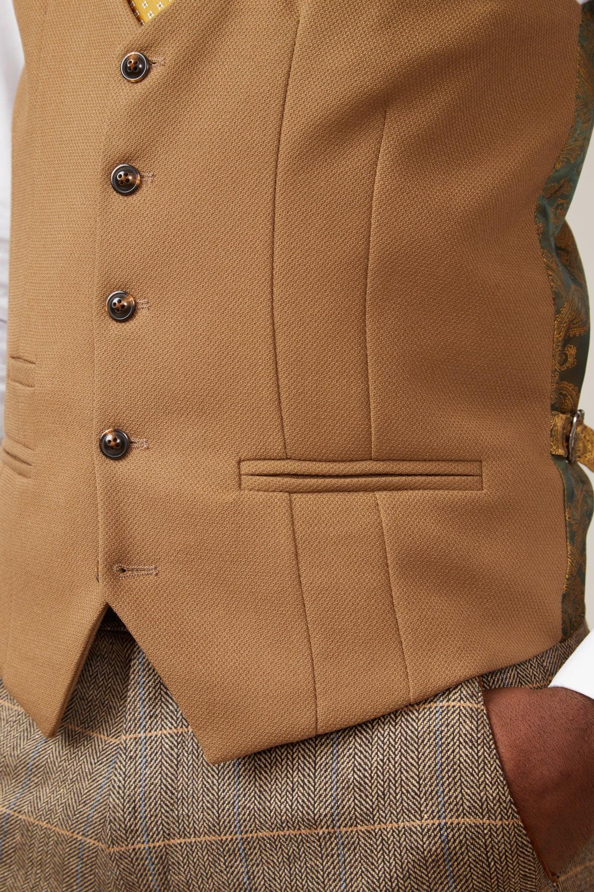 A close-up shows a person wearing the marcdarcy KELVIN - Oak Single Breasted Waistcoat over a white shirt, paired with slim fit brown plaid trousers. The back of the waistcoat features green and gold patterned fabric.