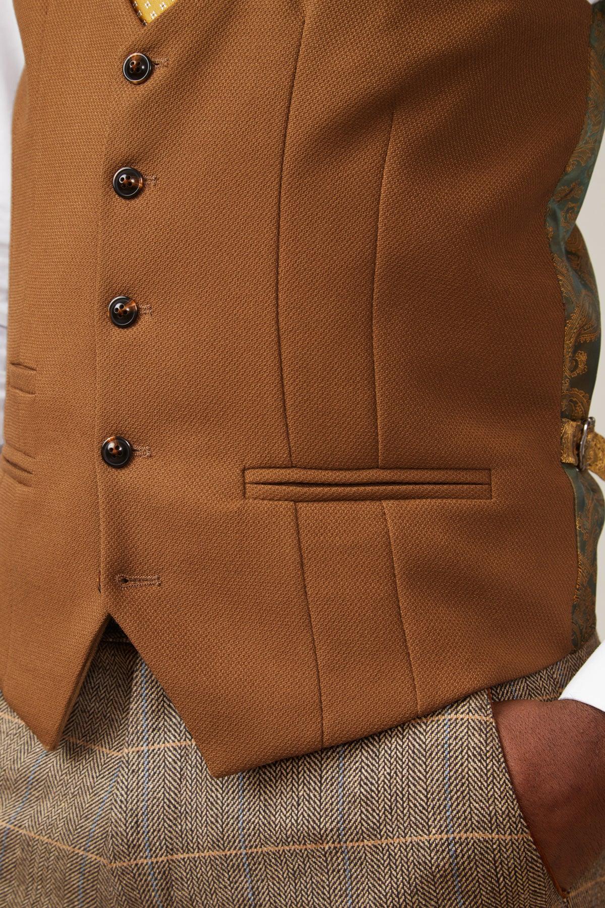 A close-up of a person wearing the marcdarcy KELVIN Tan Single Breasted Waistcoat over a white shirt, paired with plaid trousers. Their hand is in their pocket, revealing part of the paisley print lining.