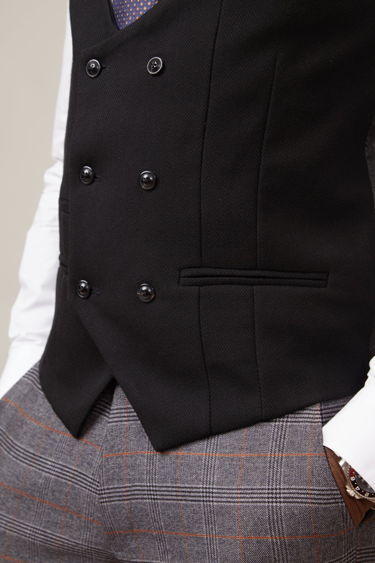 Close-up of a man wearing the marcdarcy KELVIN black double breasted waistcoat over a white shirt and grey plaid pants with orange pinstripes, accessorized with a wristwatch.