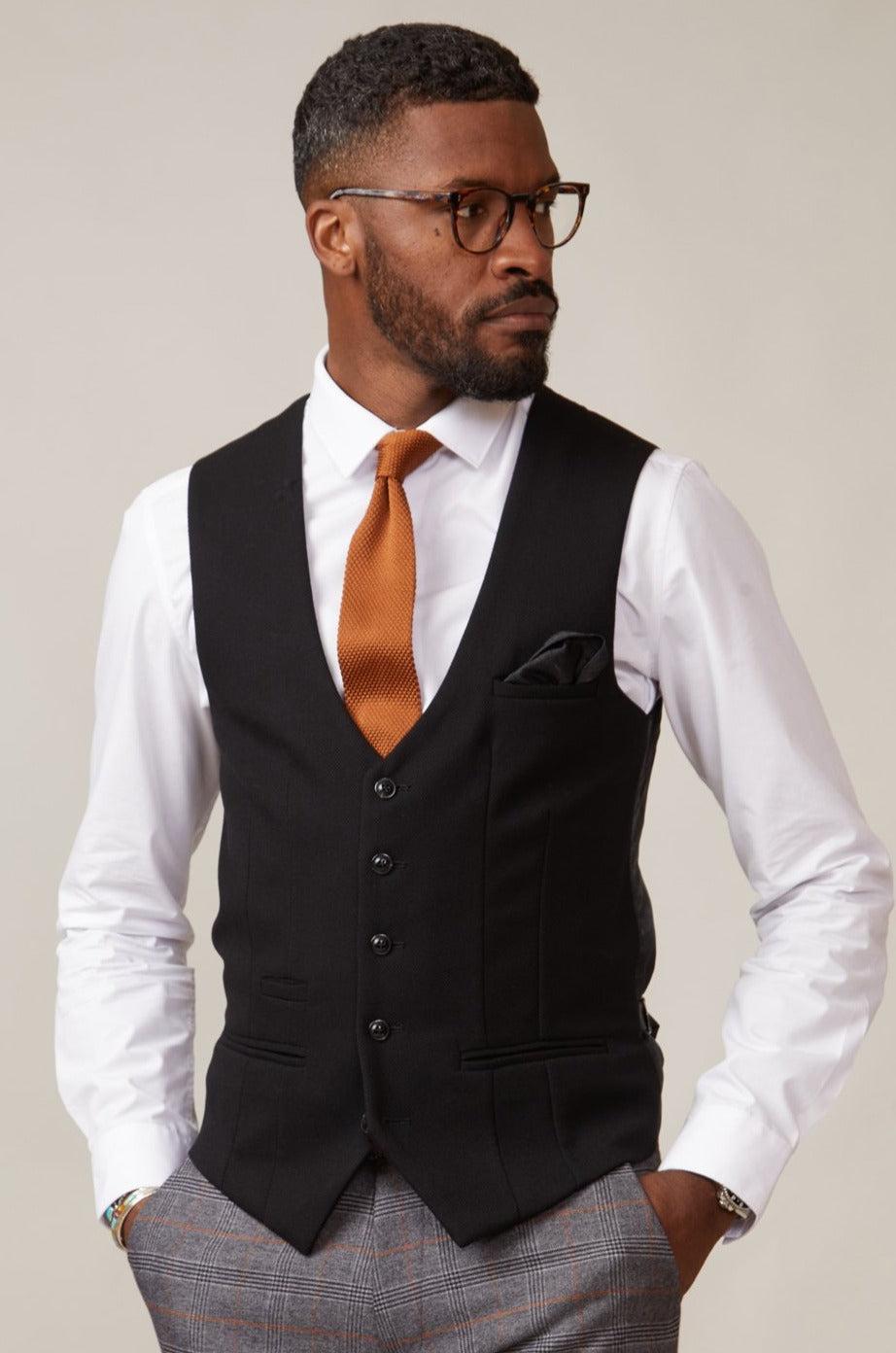 A man with glasses and a beard wears the marcdarcy KELVIN black single breasted waistcoat, featuring a paisley lining, over a white dress shirt and an orange knit tie.