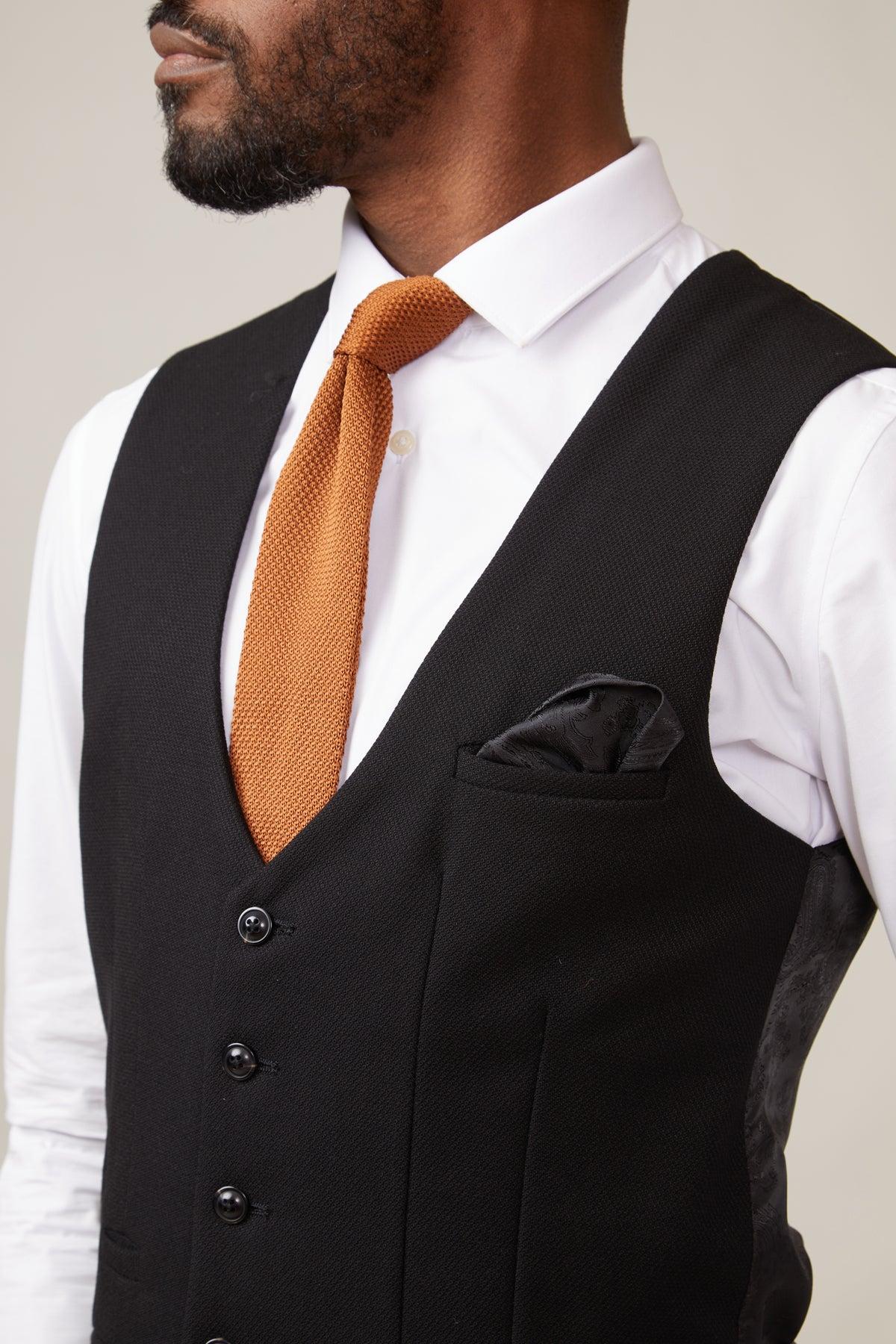 The marcdarcy KELVIN Black Single Breasted Waistcoat features paisley lining and pairs perfectly with a white shirt, orange knit tie, and black pocket square for a sharp, modern look.
