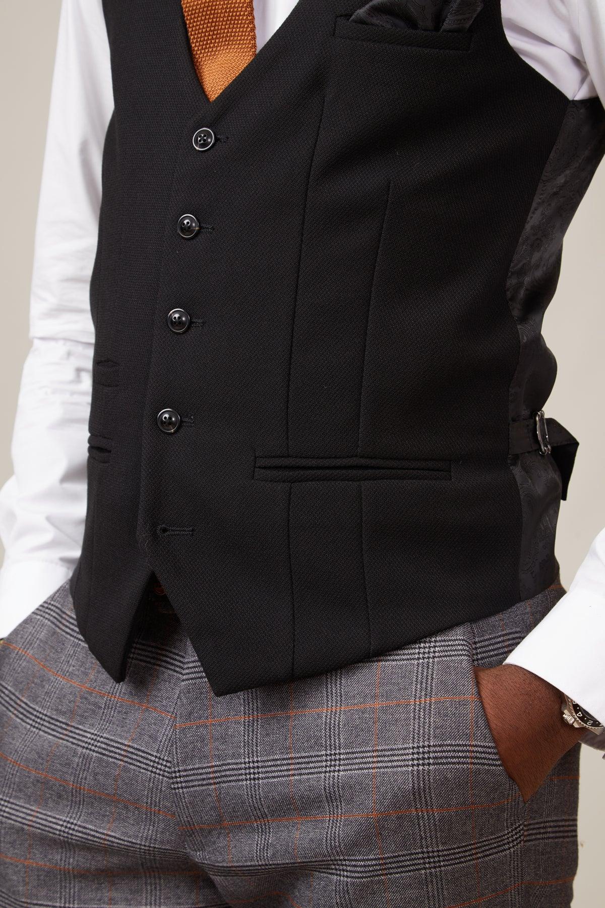 A man wears the marcdarcy KELVIN Black Single Breasted Waistcoat with a paisley lining over a white shirt and orange tie, paired with grey plaid pants featuring an orange windowpane pattern.