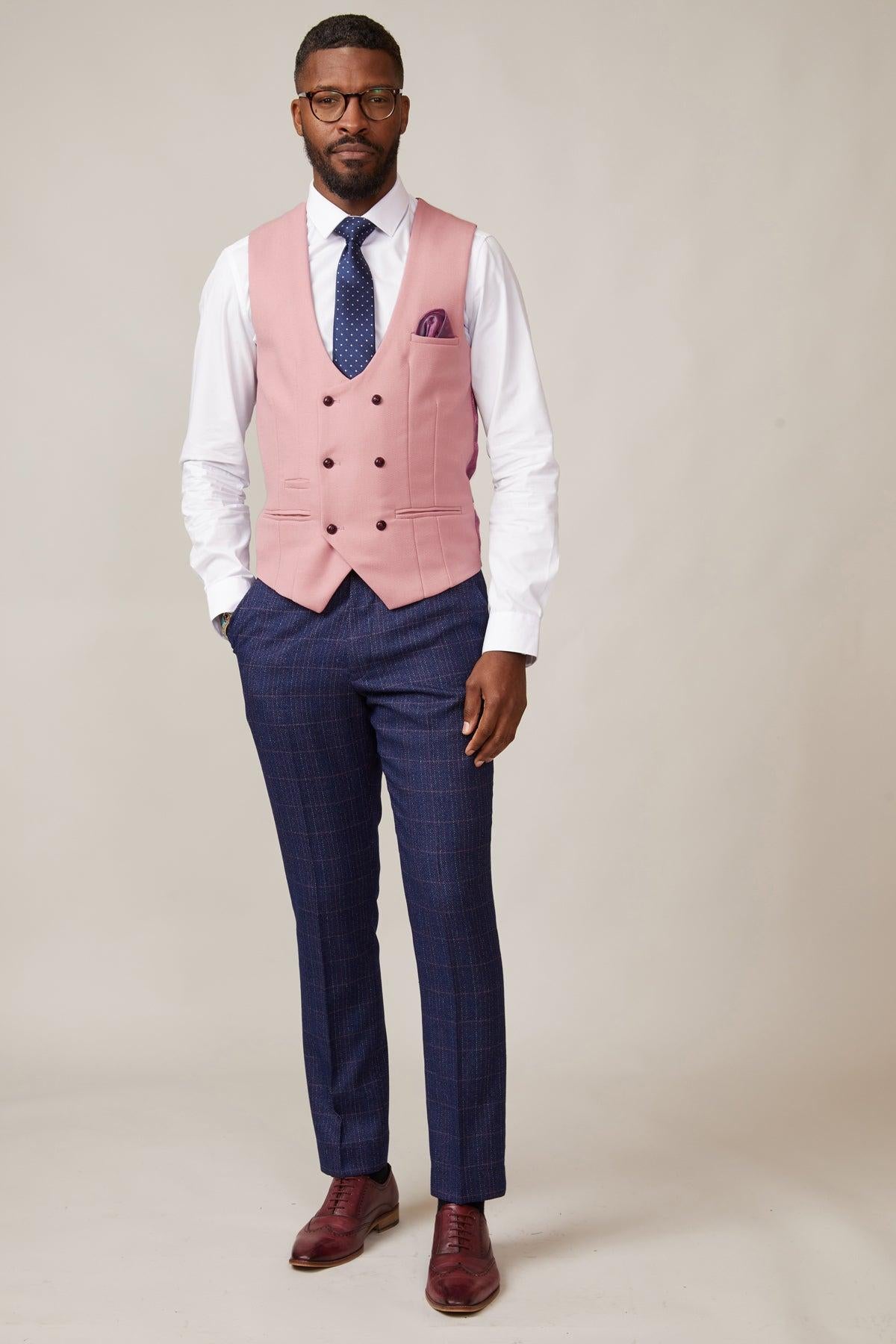 A man stands facing forward, wearing a white shirt, blue checkered trousers, a blue tie, burgundy dress shoes, and the marcdarcy KELVIN - Pink Double Breasted Waistcoat with matching pocket square. He has short hair and glasses.