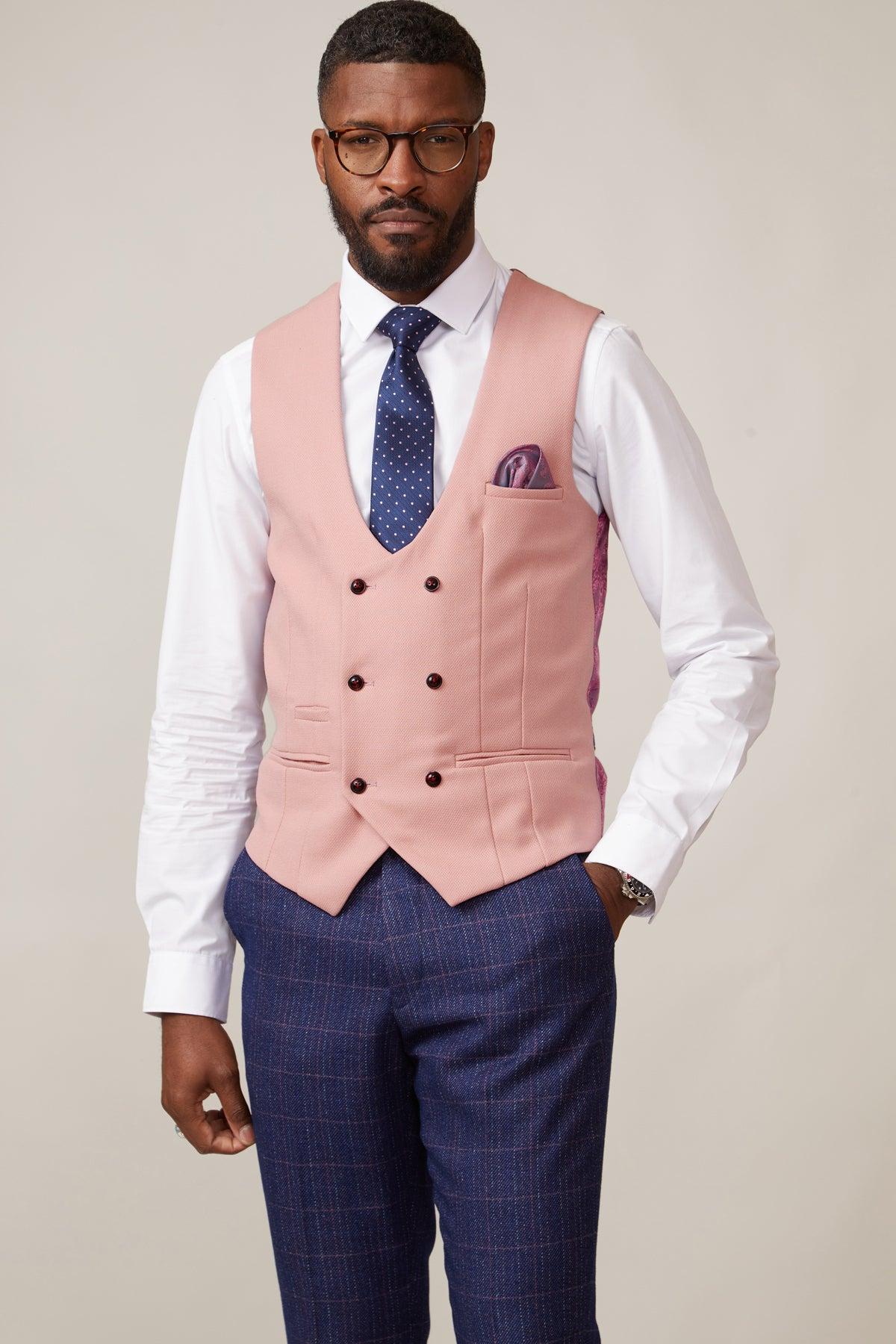 A man wears the marcdarcy KELVIN Pink Double Breasted Waistcoat with a white shirt, navy patterned tie, pocket square, and blue plaid trousers, standing against a light gray background.