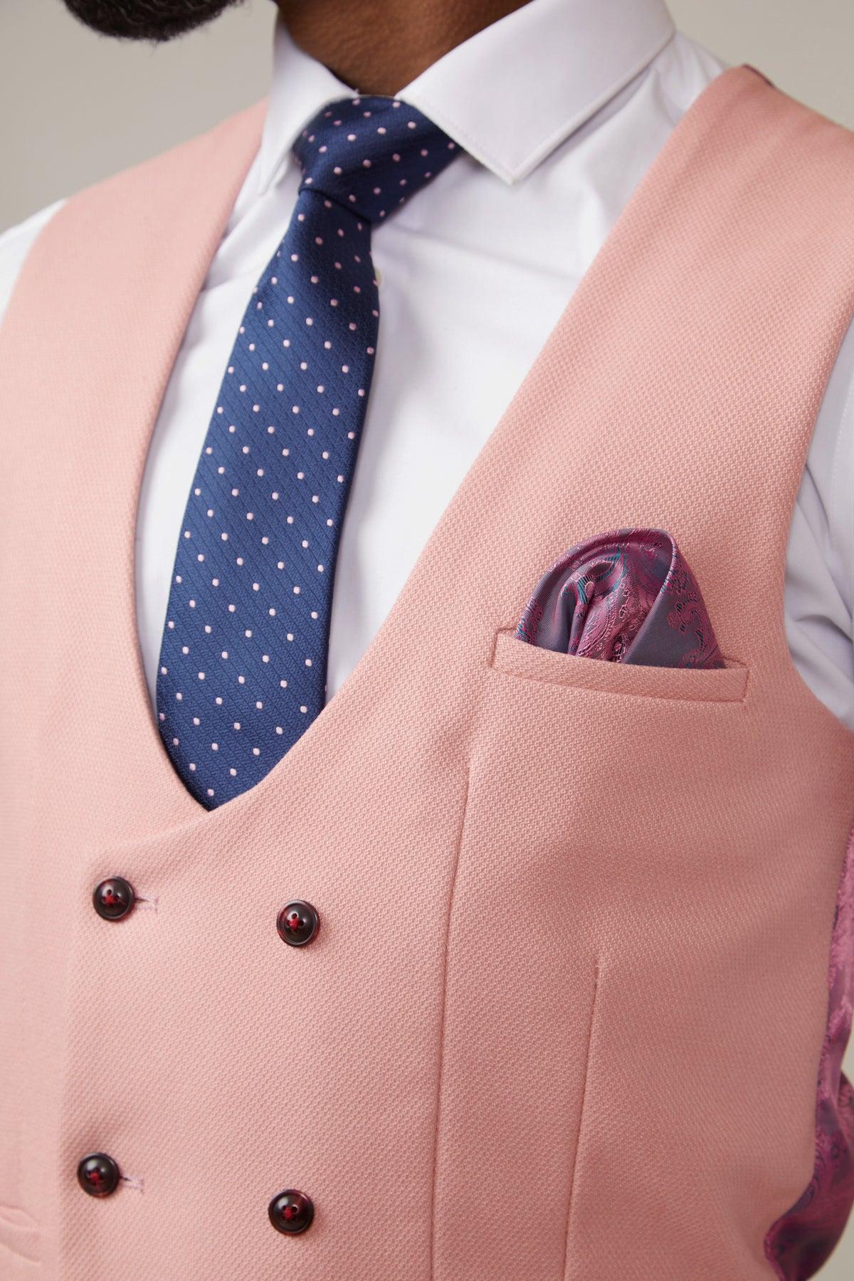 A man wears a white shirt, blue polka dot tie, and the marcdarcy KELVIN Pink Double Breasted Waistcoat with dark buttons. A purple patterned pocket square accents the look. Only his torso and part of his face are visible.