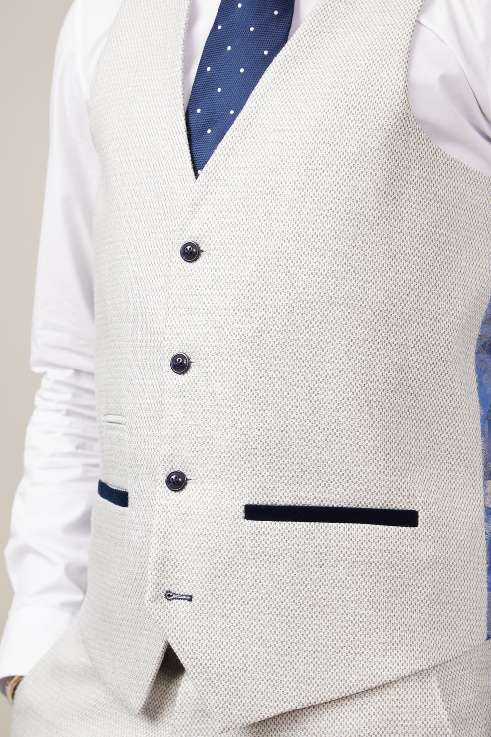 A man wears the marcdarcy RONALD - Stone Single Breasted Waistcoat with navy trim and buttons, styled with a white penny collar shirt and a navy polka dot tie.