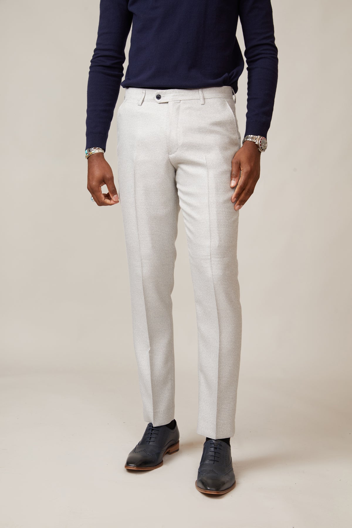 A person wears a navy long-sleeve shirt, marcdarcy RONALD Stone Tailored Trousers, and black dress shoes while standing against a plain beige background. The person's head is not visible in the image.