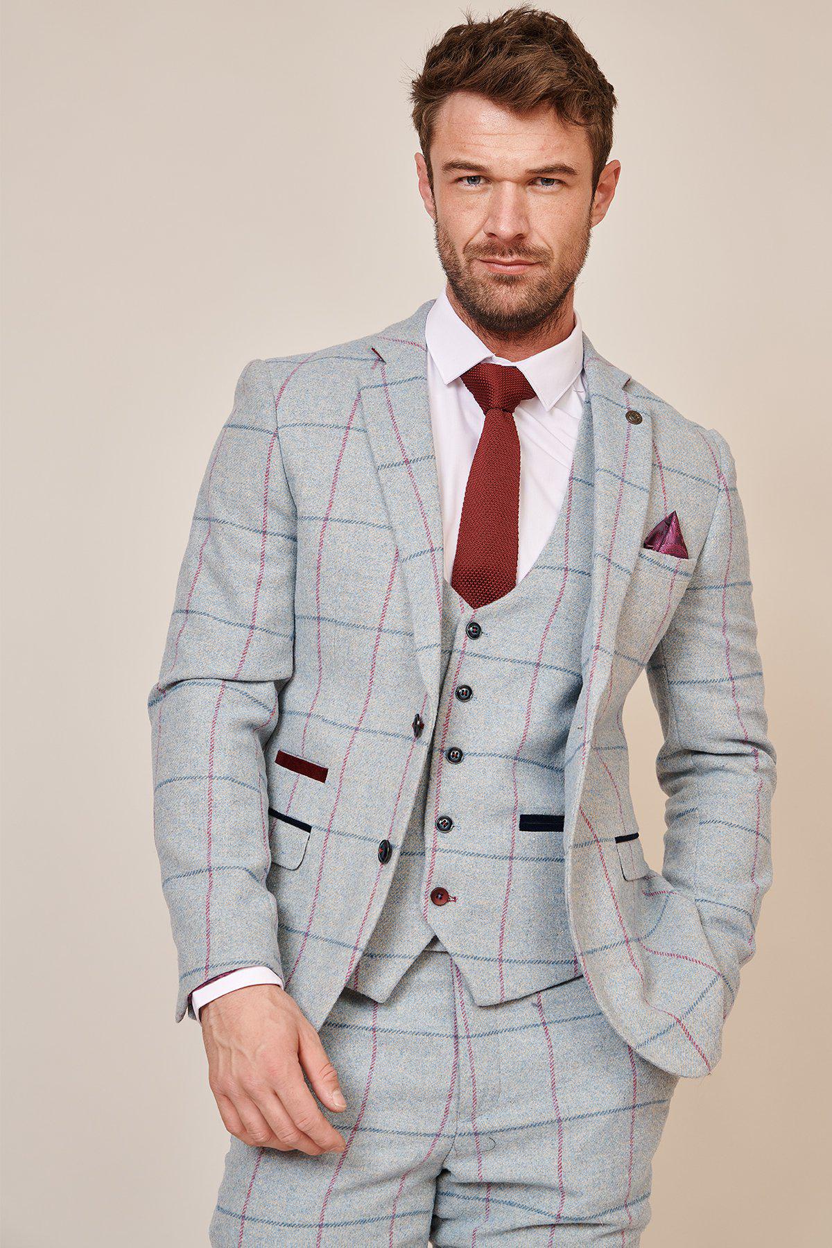 A man wears the Marc Darcy NICOLAS - Sky Check Tweed Blazer with a white shirt, red tie, and matching waistcoat, standing confidently with one hand in his pocket and looking at the camera.