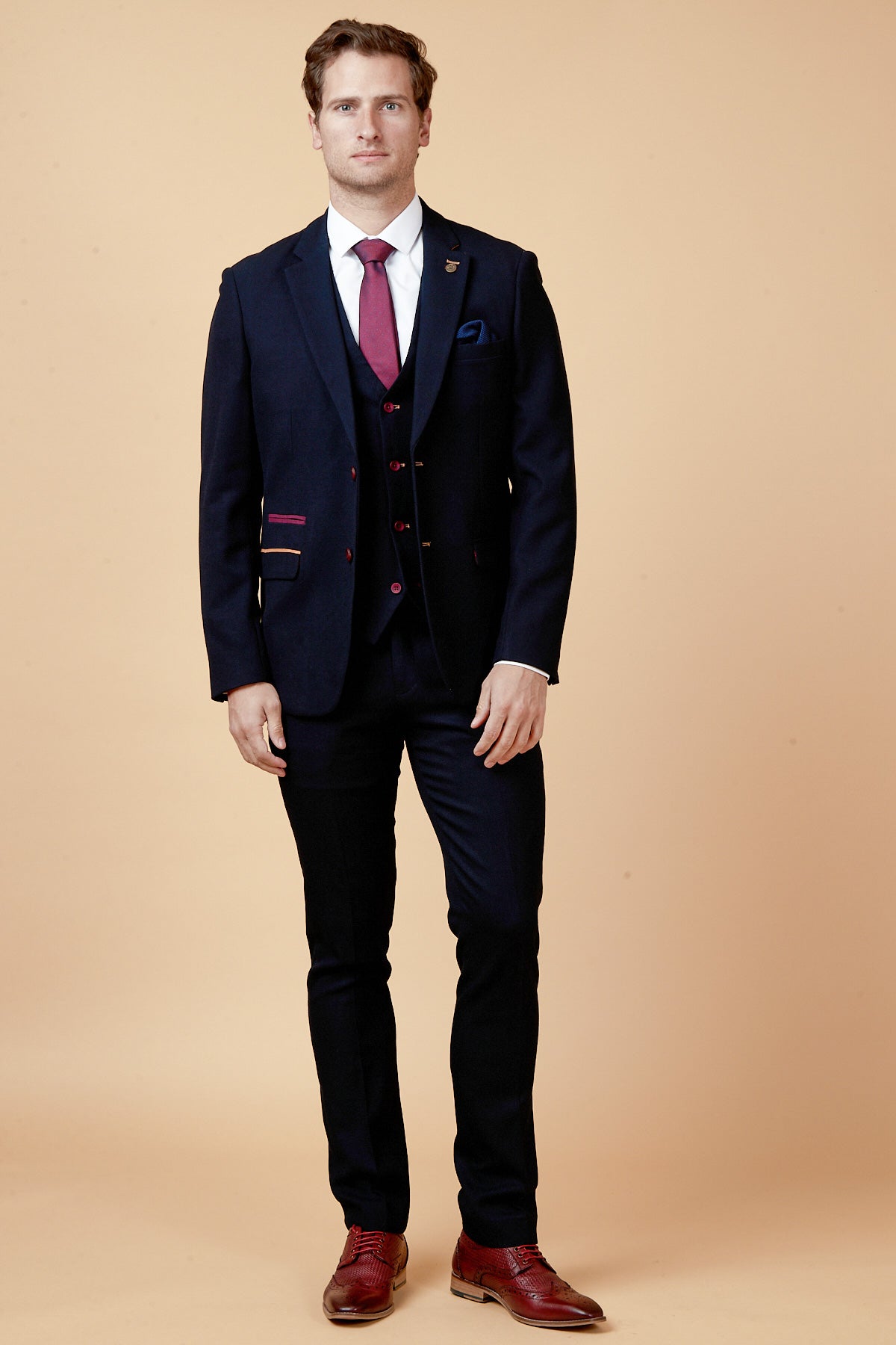 A man wears the marcdarcy JD4 - Navy Contrast Trim Three Piece Suit with matching vest, burgundy tie and pocket square, and red dress shoes—perfect attire for a wedding guest.