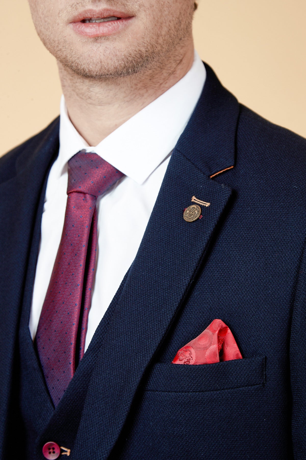 A man wears the marcdarcy JD4 Navy Contrast Trim Three Piece Suit with a slim fit, white dress shirt, and red tie plus matching pocket square. The textured suit features a lapel pin, ideal for a stylish wedding guest look. His face is partially visible.