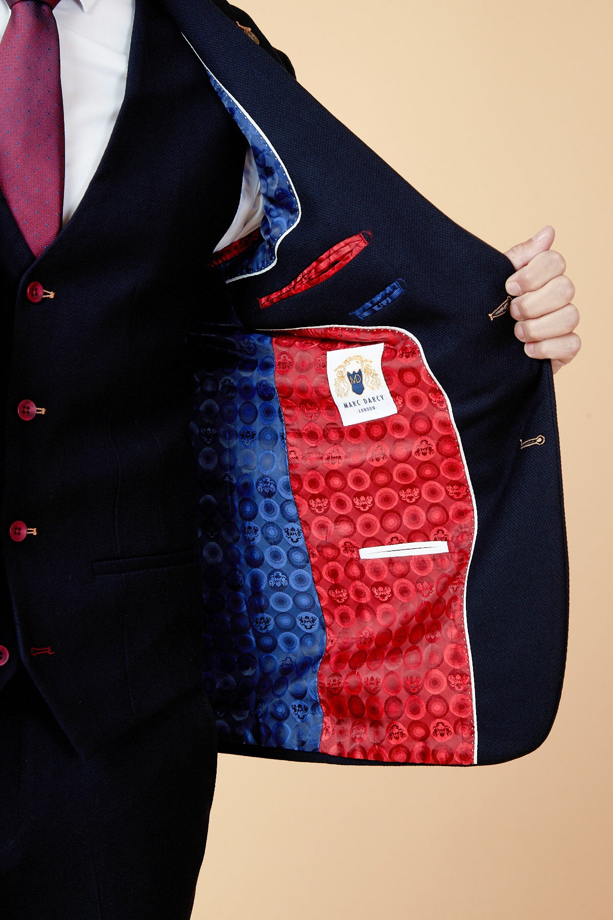 A person in a marcdarcy JD4 - Navy Contrast Trim Three Piece Suit holds open their jacket to reveal a colorful skull-patterned lining—blue on one side, red on the other—with a visible designer label inside this slim-fit suit.