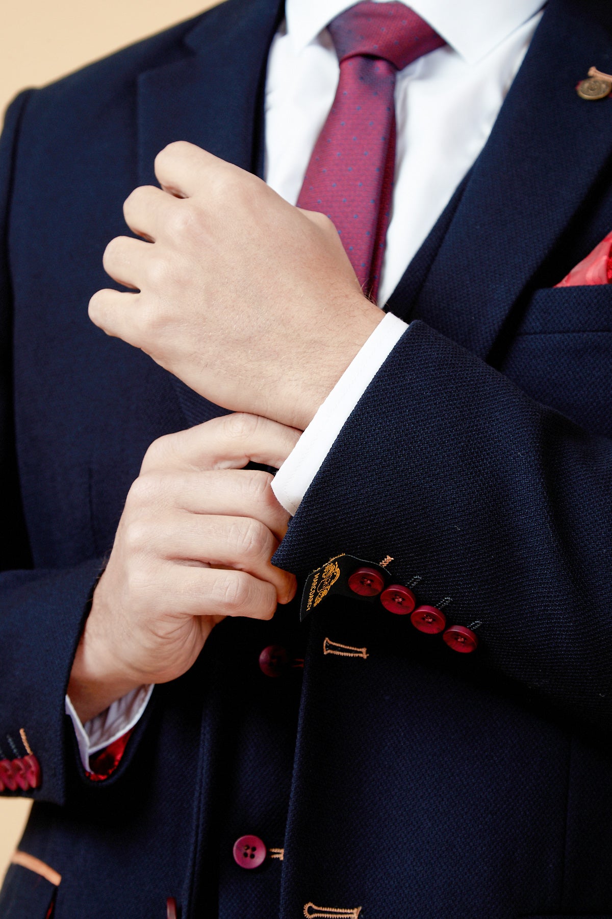 A man adjusts his marcdarcy JD4 - Navy Contrast Trim Blazer, revealing a white shirt, red polka-dot tie, and red pocket square. The slim fit blazer features gold embroidery, red buttons, and a paisley lining.