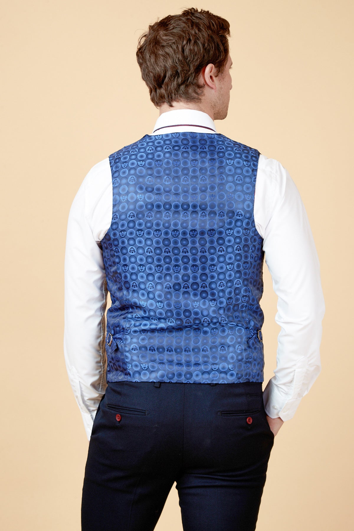 A man faces away, wearing a white dress shirt, dark trousers, and the marcdarcy JD4 - Navy Contrast Trim Waistcoat with circular patterns. This slim fit outfit pops against a plain beige background.