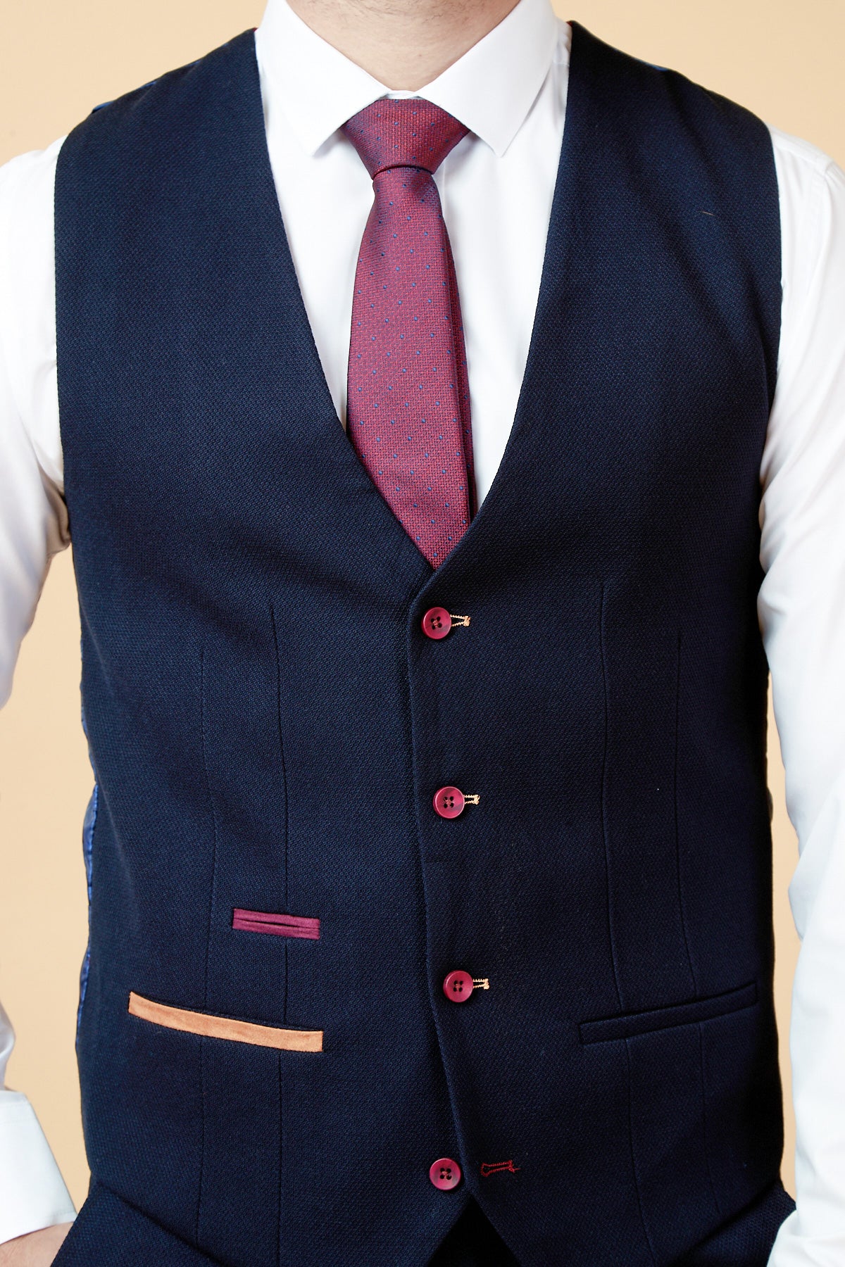 A man in the marcdarcy JD4 Navy Contrast Trim Waistcoat with red buttons and colorful pocket trims, paired with a slim fit white shirt and red patterned tie, shown waist up against a beige background.