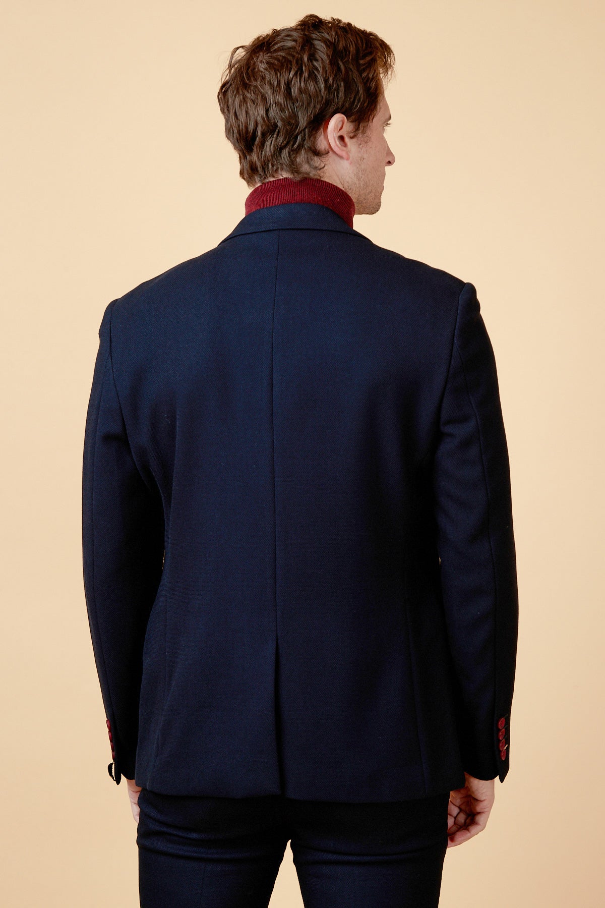 A man with short brown hair stands with his back to the camera, wearing the marcdarcy JD4 - Navy Contrast Trim Blazer and a maroon turtleneck, creating an elegant workwear look against a plain beige background.