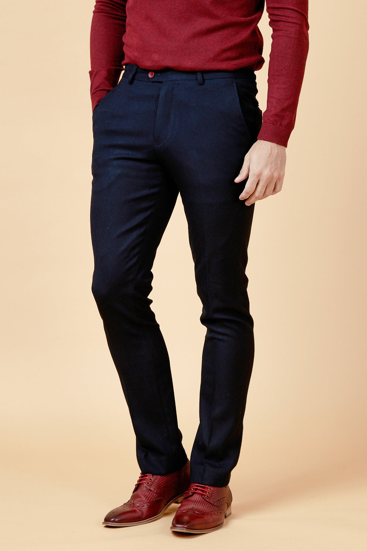 Man wearing a fitted maroon sweater with burgundy buttons, JD4 - Navy Flat Front Trousers by marcdarcy, and burgundy oxford shoes, standing against a plain beige background. His head is not visible in the image.