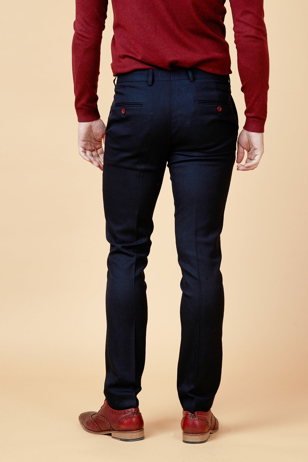 A person stands facing away in a slim fit red long-sleeve shirt with burgundy buttons, marcdarcy JD4 - Navy Flat Front Trousers, and brown dress shoes against a plain beige background.