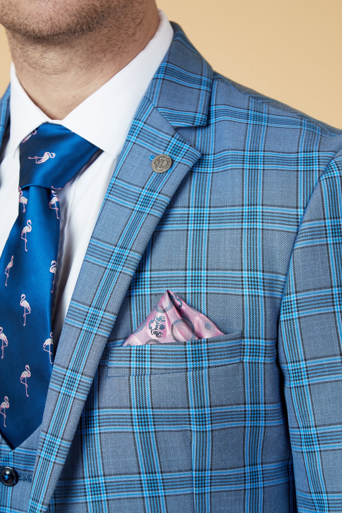 Close-up of a man's torso wearing the Marc Darcy JOSE - Sky Blue Check Blazer in a tailored fit, paired with a white shirt, blue tie with pink flamingos, and a pink patterned pocket square against a beige background.