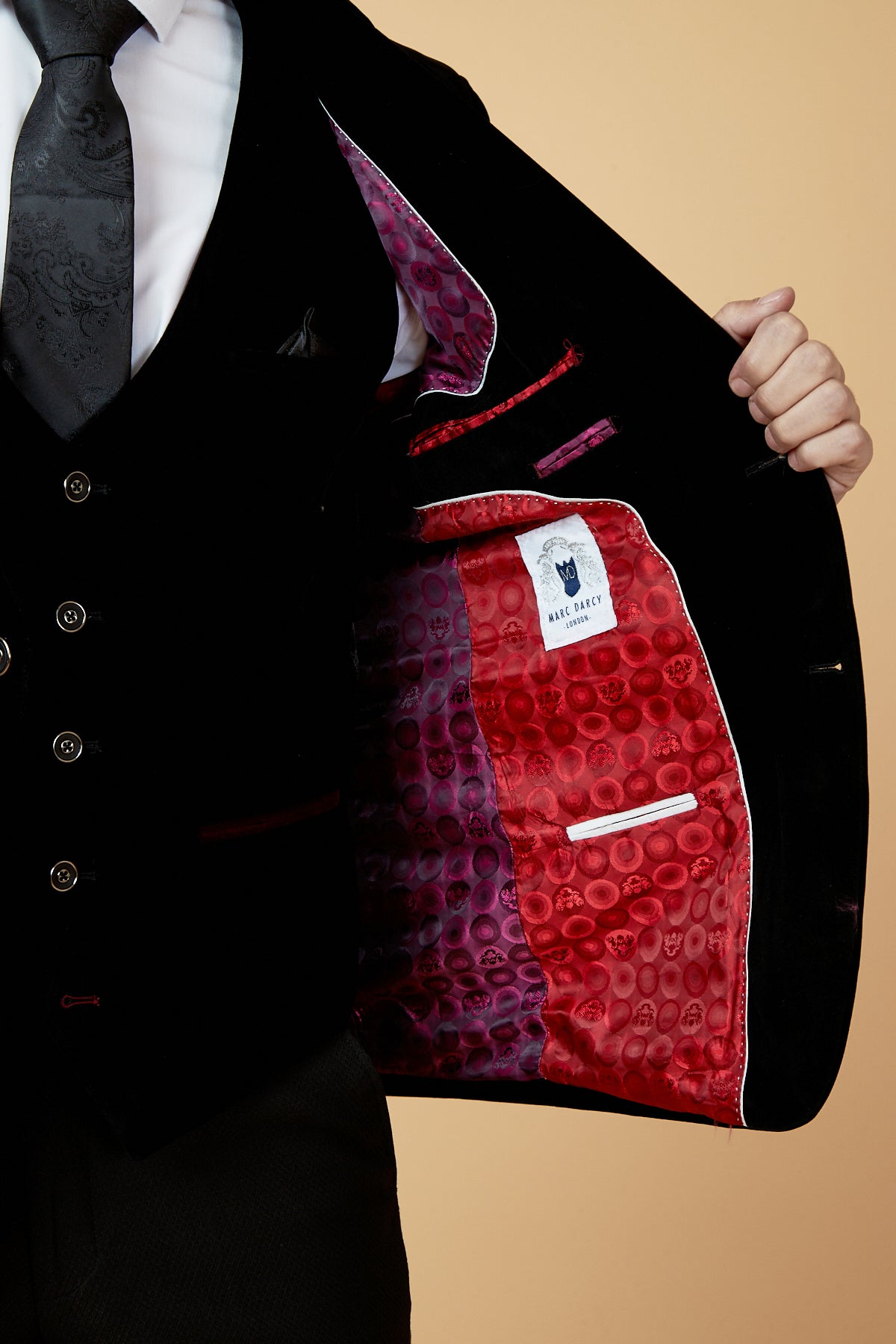 Wearing the marcdarcy HUDSON Black Velvet Blazer, a person in black tie opens their jacket to reveal a vibrant red and purple circular patterned lining and a white “MAKE GREECY” label.