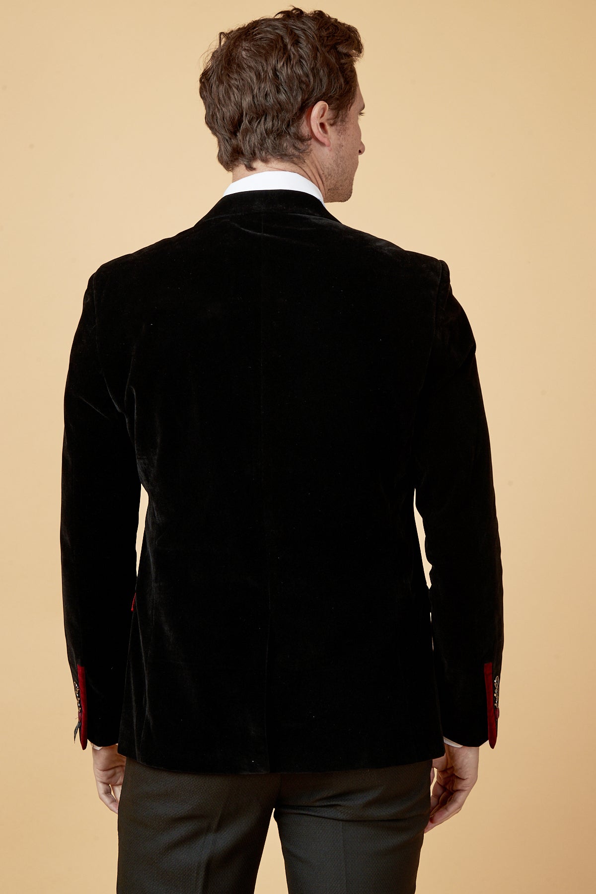 A man with short brown hair is seen from behind wearing the marcdarcy HUDSON Black Velvet Blazer over a white shirt and dark trousers, set against a plain beige background.