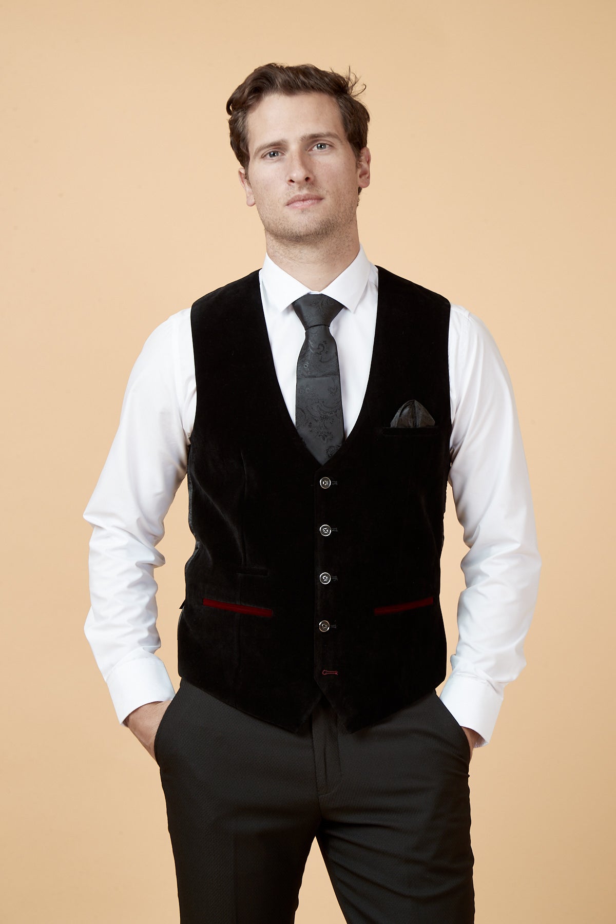 A man stands facing the camera, one hand in his pocket, wearing a white shirt, dark pants, a black patterned tie, and the marcdarcy HUDSON Black Velvet Jacquard Waistcoat.
