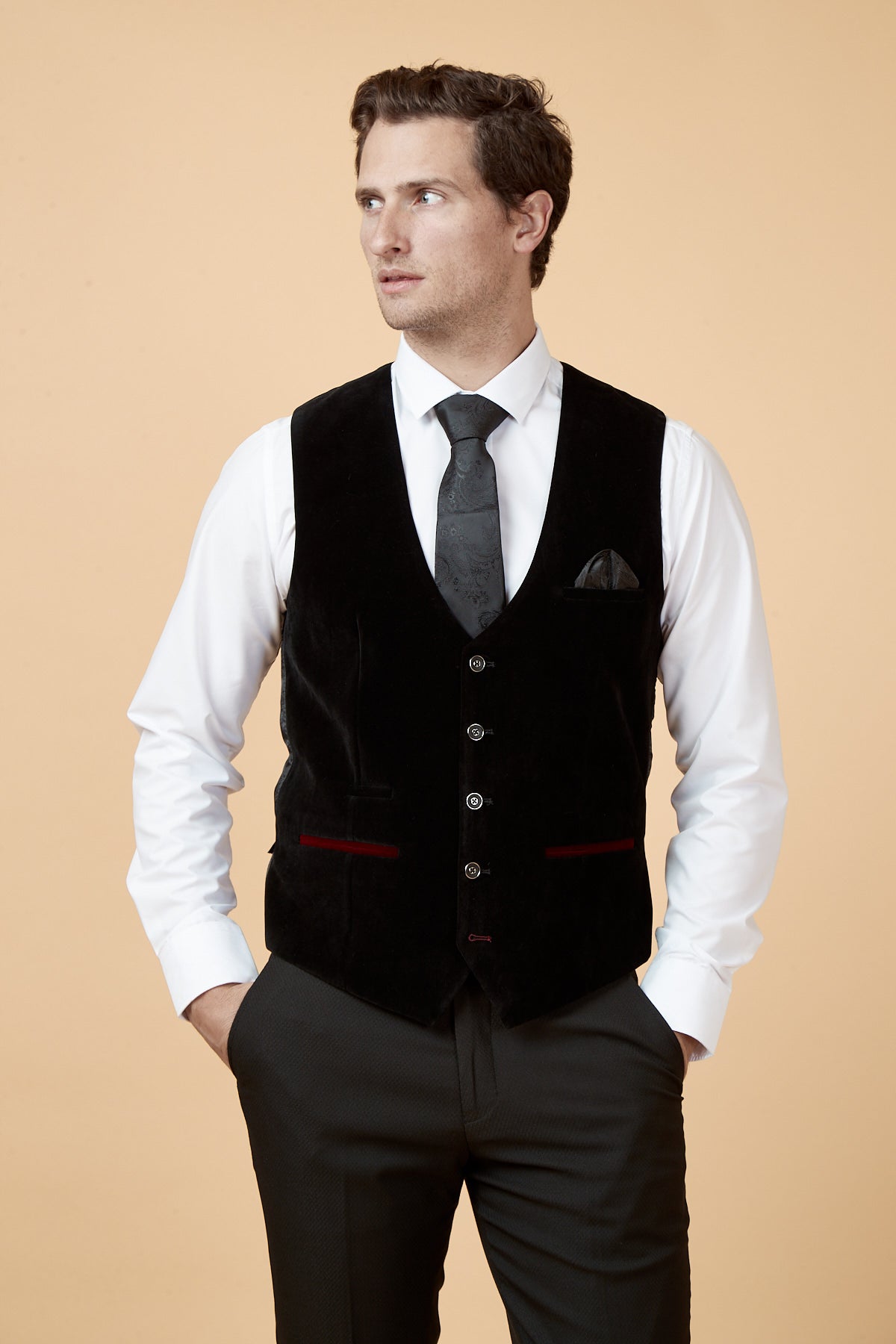 A man in a marcdarcy HUDSON black velvet jacquard waistcoat, white shirt, black patterned tie, and grey patterned trousers.