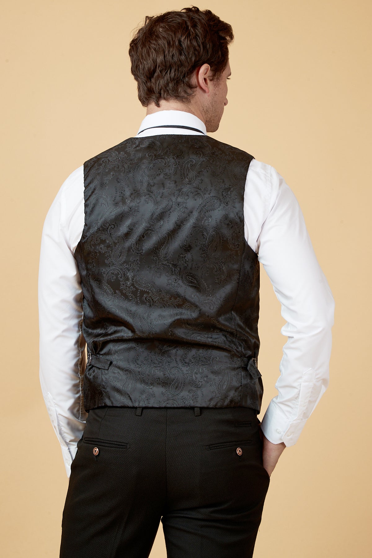 Back view of a man in the marcdarcy HUDSON Black Velvet Jacquard Waistcoat, styled with a white dress shirt and tailored black patterned trousers.