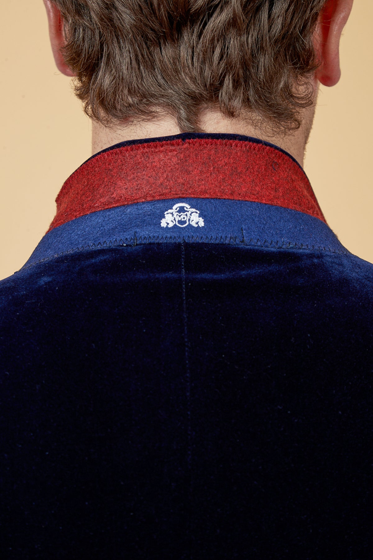 Close-up of the back of a man’s neck wearing the marcdarcy HUDSON Navy Velvet Blazer, featuring a red inner collar lining and a small white embroidered emblem at the center.