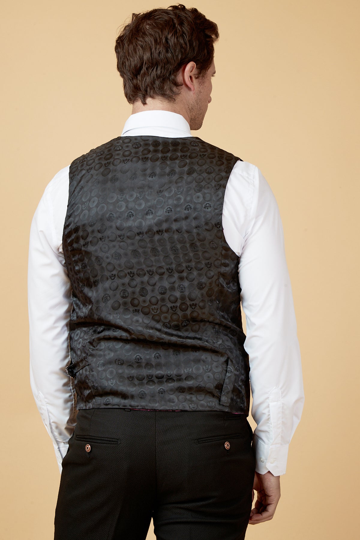 A man is seen from the back wearing a white dress shirt, black trousers, and the marcdarcy HUDSON Navy Velvet Jacquard Waistcoat with a subtle circular pattern, standing against a beige background.