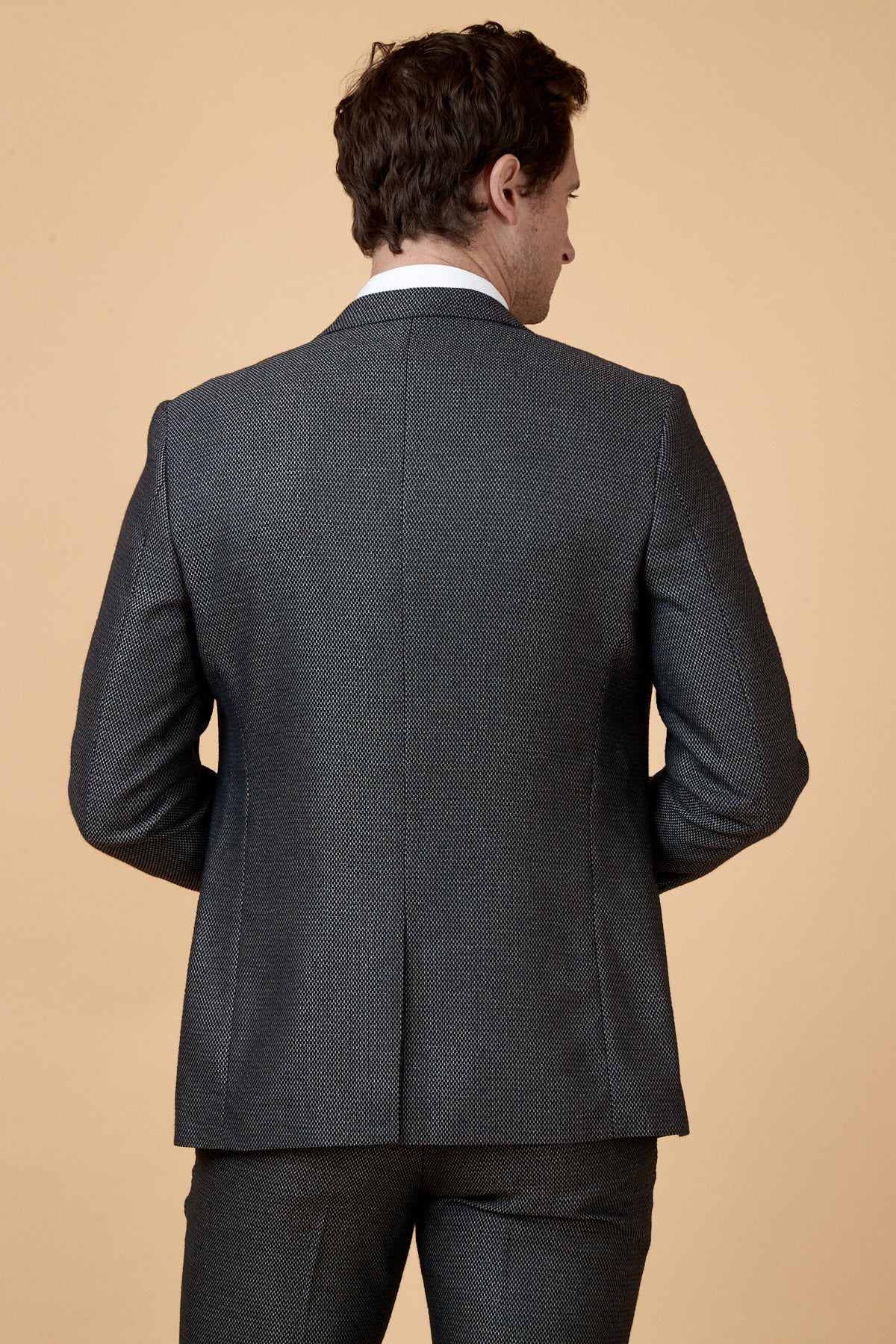 Rear view of a man in the marcdarcy SPENCER Charcoal Grey Tux Lapel Blazer, slim fit and tailored for a refined silhouette, set against a tan background.