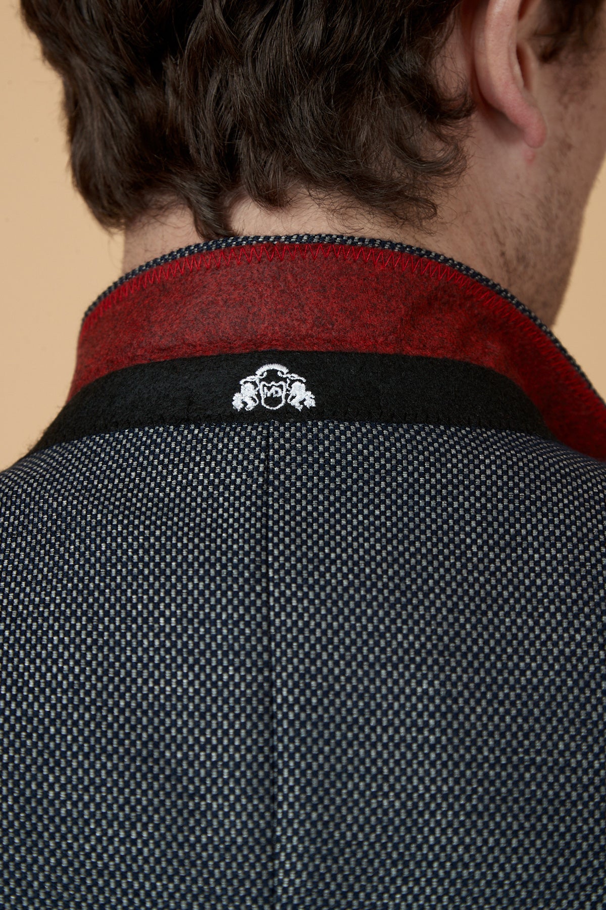 Close-up of a man's neck and shoulders in the marcdarcy SPENCER Charcoal Grey Tux Lapel Blazer, featuring a slim fit, textured finish, red and black collar detail, and white embroidered logo—ideal for formal or black tie events.