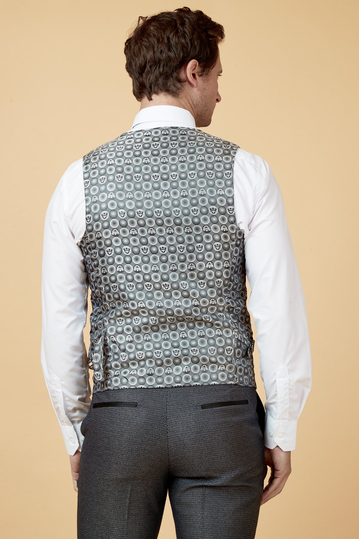 A man faces away, wearing a white shirt, dark gray trousers, and the marcdarcy SPENCER Charcoal Grey Single Breasted Waistcoat—ideal for formal occasions—set against a plain beige background.