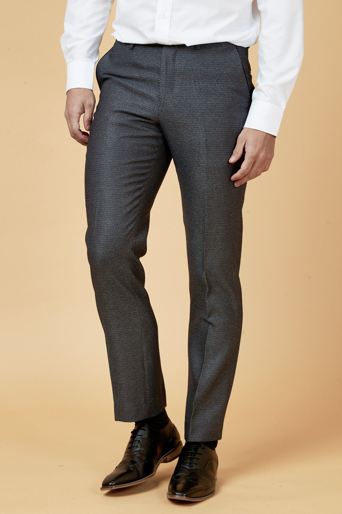 A person wears marcdarcy’s SPENCER Charcoal Grey Trousers with a white shirt and black dress shoes against a beige background. The image, cropped at the shoulders, showcases attire ideal for formal occasions.