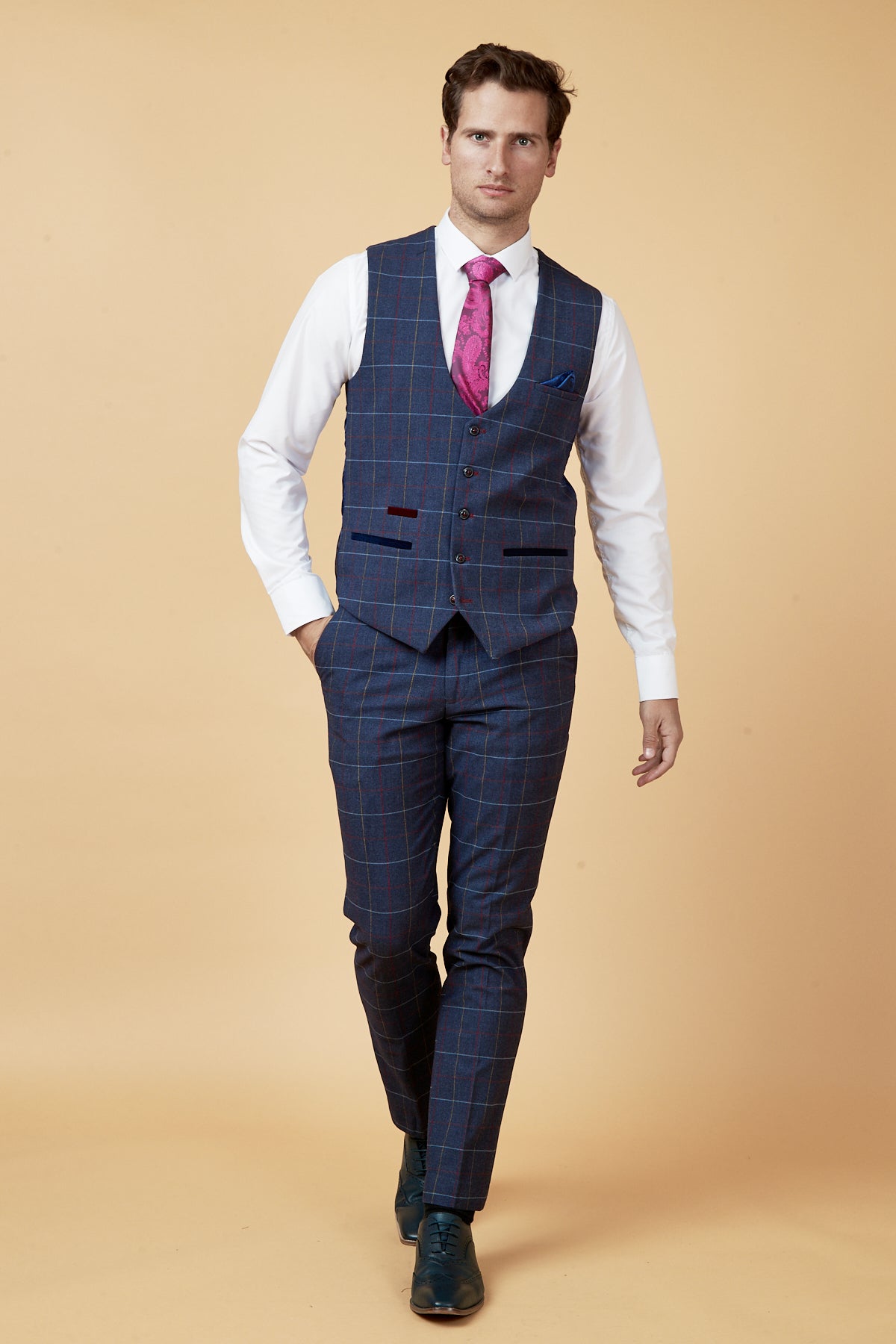 A man in the marcdarcy DRAKE Navy Check Waistcoat, white shirt, matching trousers, pink tie, and dark shoes walks confidently against a beige background.