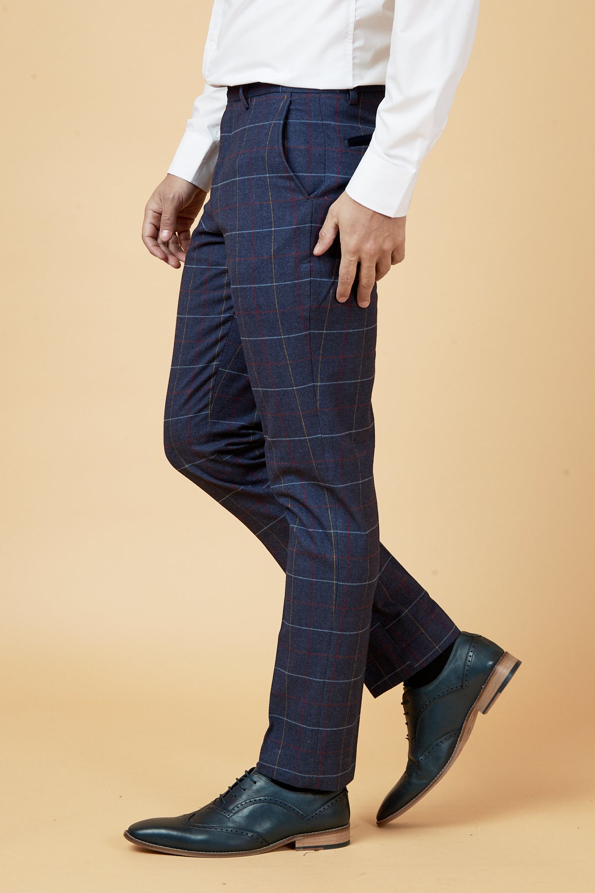 A person wearing marcdarcy’s DRAKE Navy Check Three Piece Suit, featuring slim fit plaid dress pants and a white shirt with dark blue shoes, stands against a beige background; only their lower half is visible.