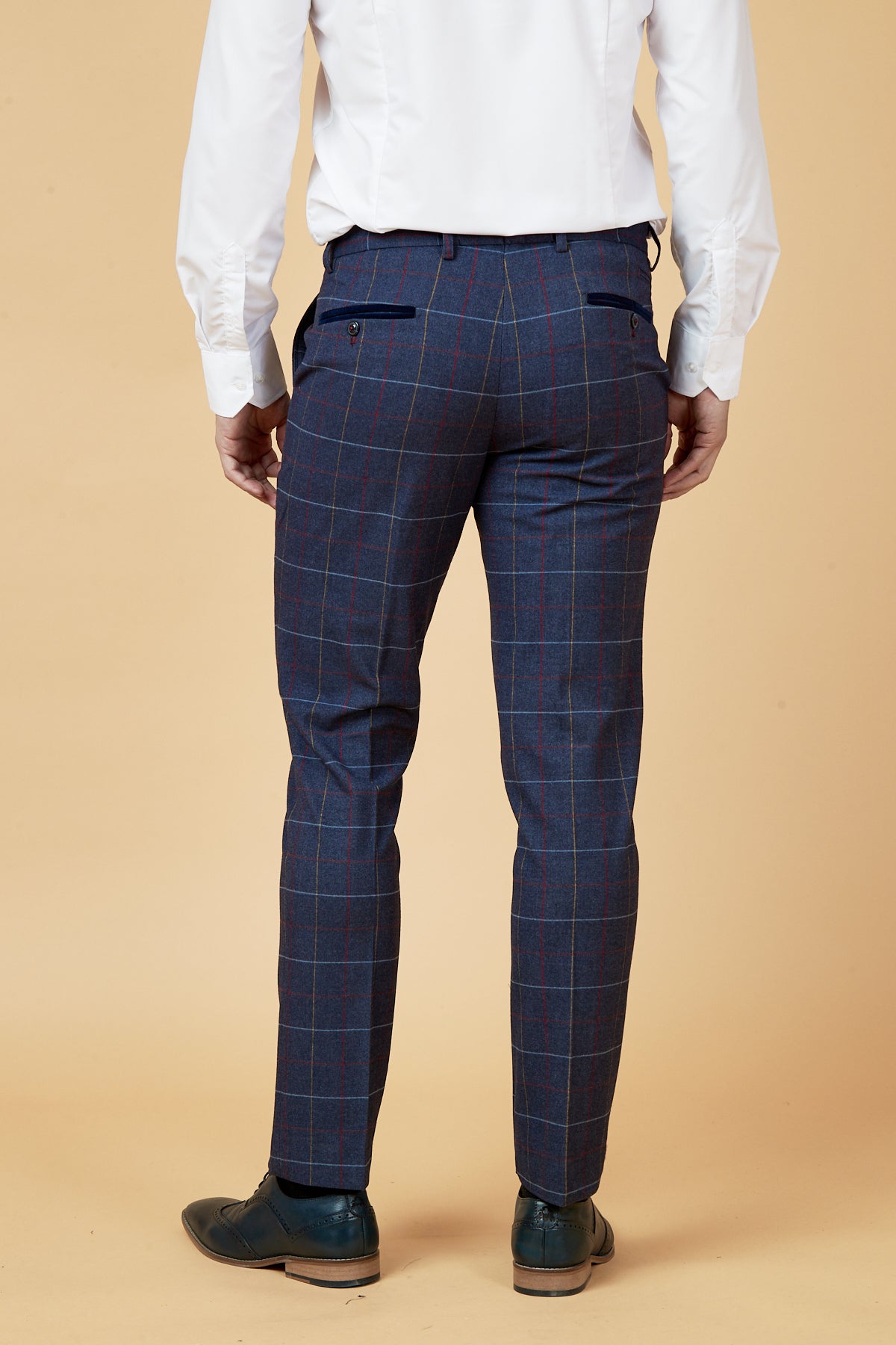 A person wearing the marcdarcy DRAKE - Navy Check Three Piece Suit faces away, arms at their sides, against a beige background. They also wear a white dress shirt and dark dress shoes.