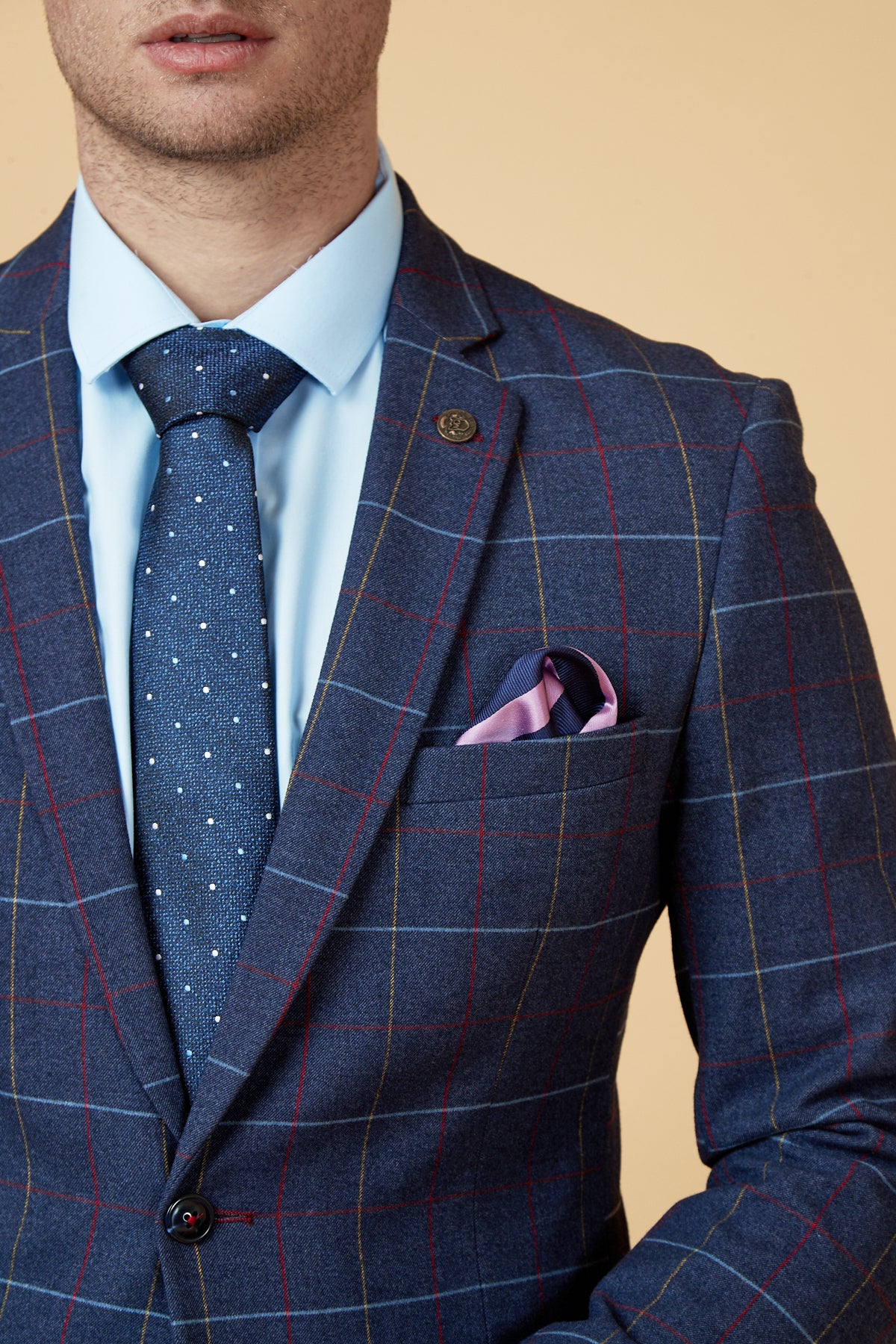 A man wears the marcdarcy DRAKE - Navy Check Blazer, styled with a light blue shirt, polka dot tie, and pink pocket square. His face is partly out of frame against a beige background.