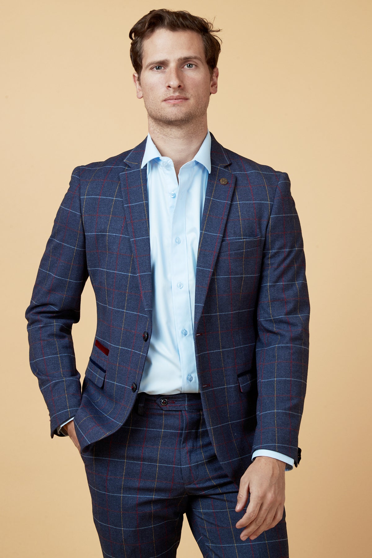 A man poses confidently against a light beige background wearing the marcdarcy DRAKE Navy Check Blazer over a light blue shirt, with one hand in his pocket.