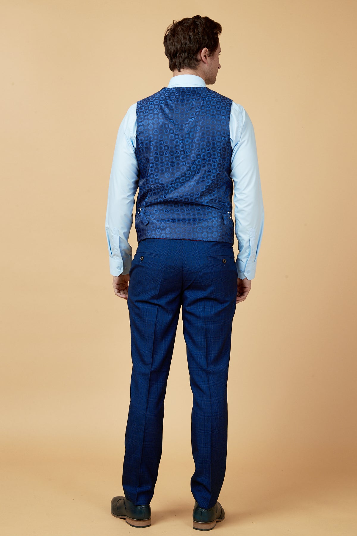 Back view of a man wearing a light blue dress shirt, marcdarcy's LEE GEORGE Royal Blue Double Breasted Waistcoat, and navy Prince of Wales check trousers.