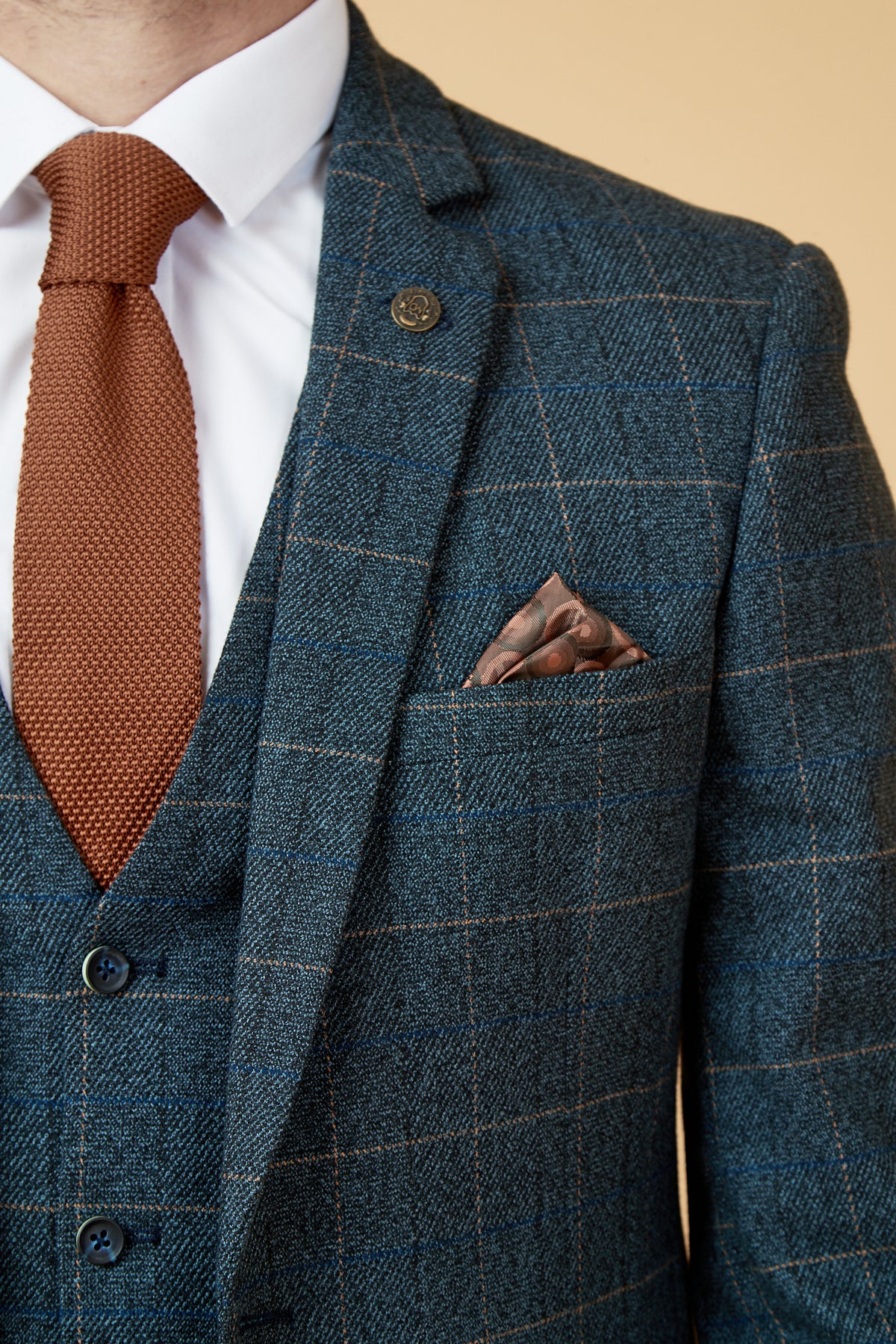 A man wears the marcdarcy SCOTT Blue Tweed Check Blazer with a brown tie, matching pocket square, white dress shirt, and bronze lapel pin. Only his upper torso, neck, and lower face are shown.